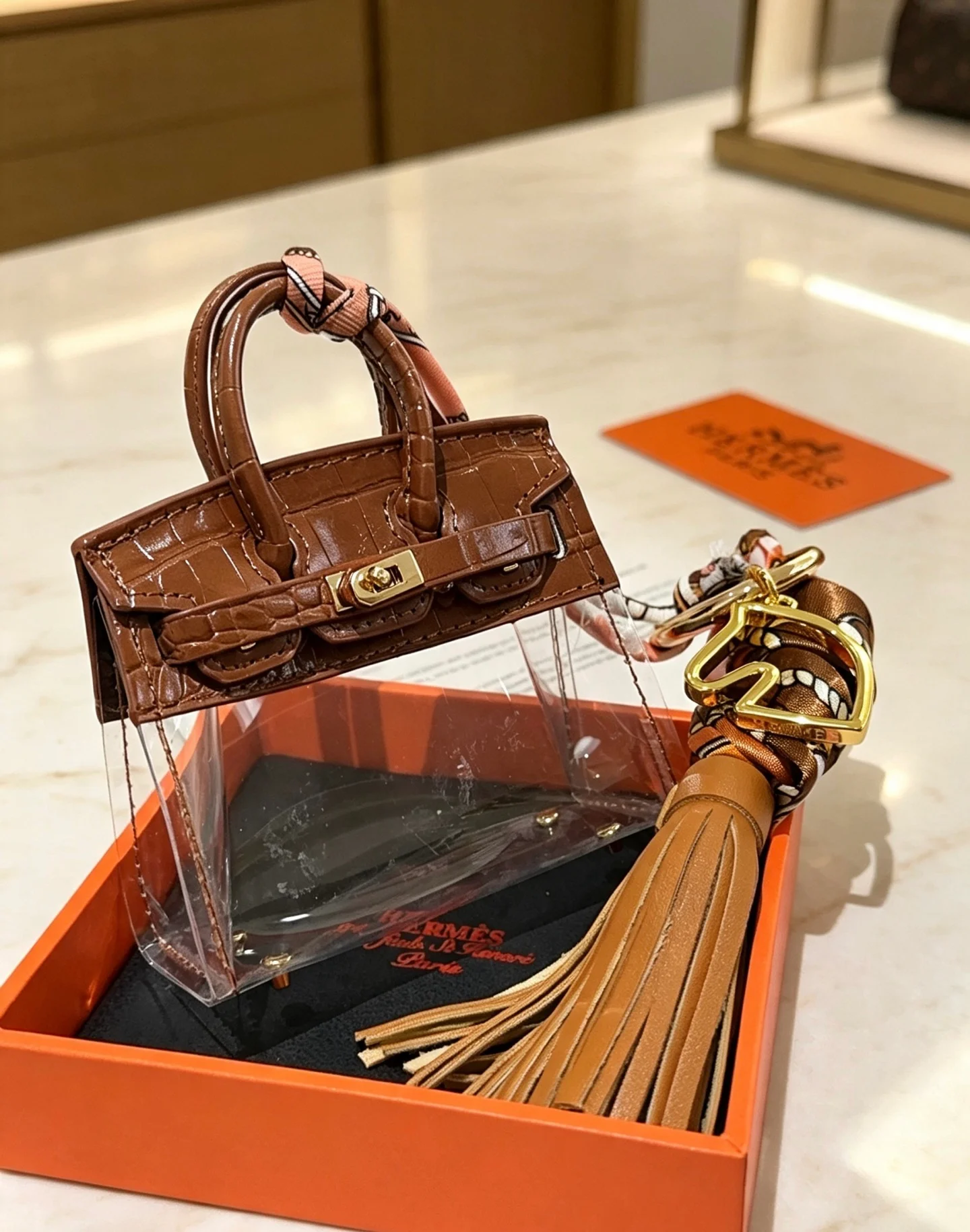 Ciondolo Hermes Birkin Micro Bag Metallo color oro pelle goffrata coccodrillo marrone PVC trasparente nappa in pelle marrone chiaro twilly di seta stampata multicolore lunghezza totale 12 cm