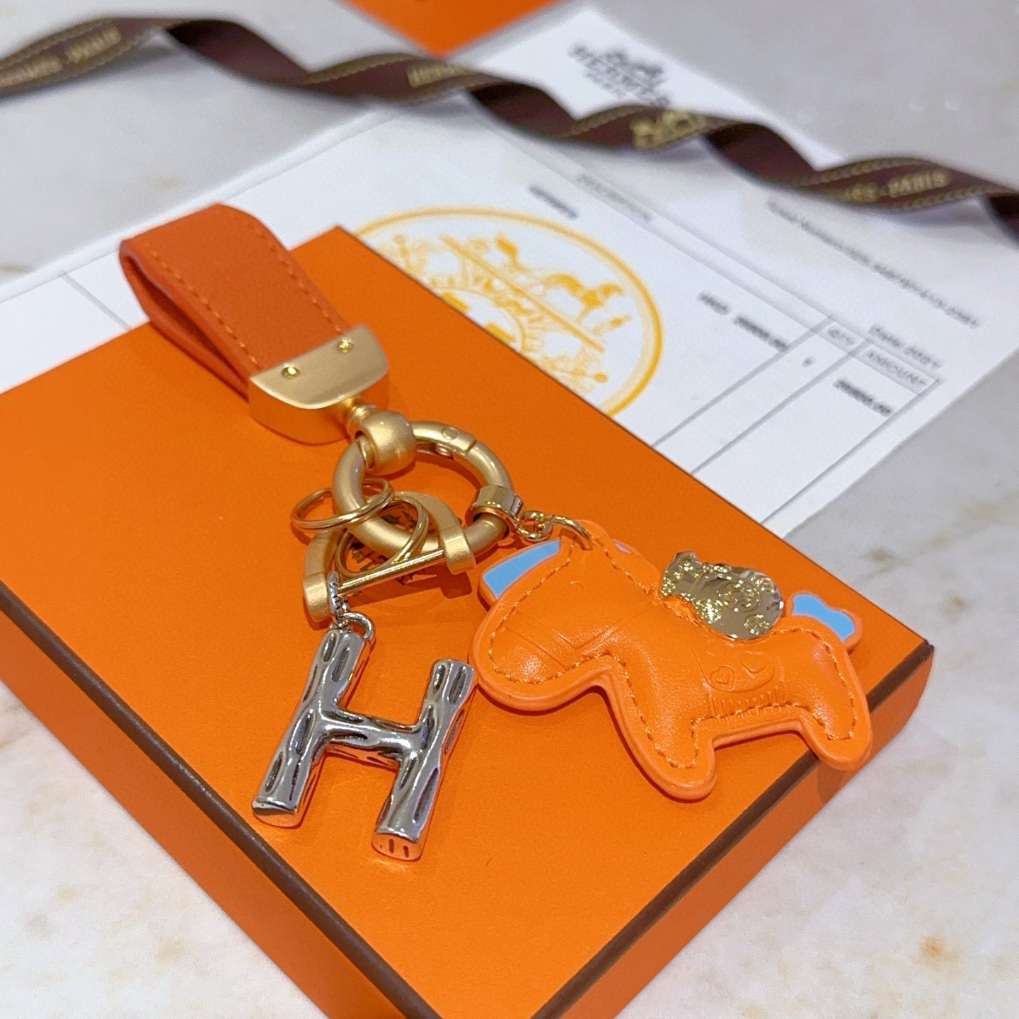 Colgante Hermes Rodeo Pegase H Logo Key Charm Cuero naranja con detalles en azul claro Herrajes metálicos en tono dorado y plateado Longitud total de 8 cm