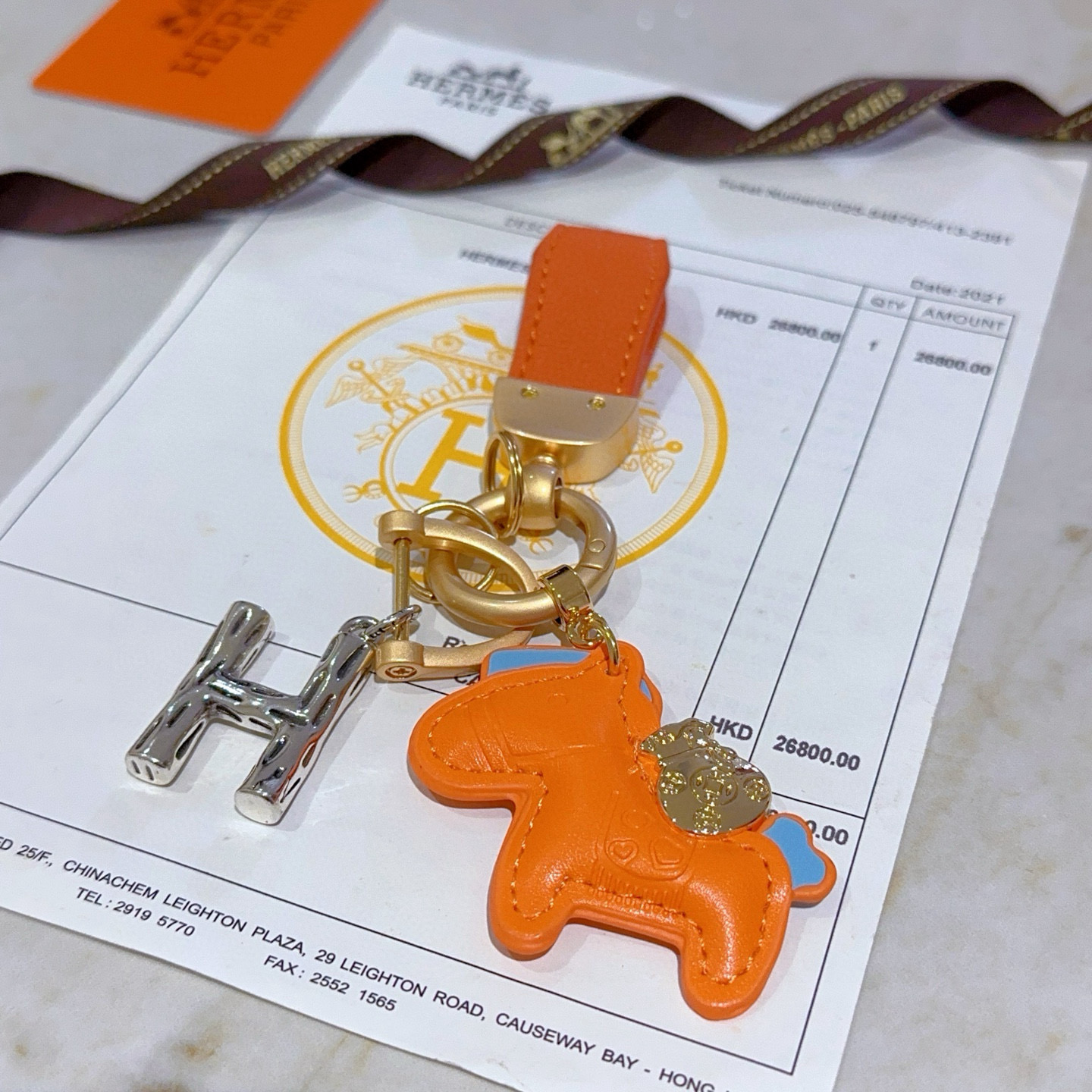 Colgante Hermes Rodeo Pegase H Logo Key Charm Cuero naranja con detalles en azul claro Herrajes metálicos en tono dorado y plateado Longitud total de 8 cm