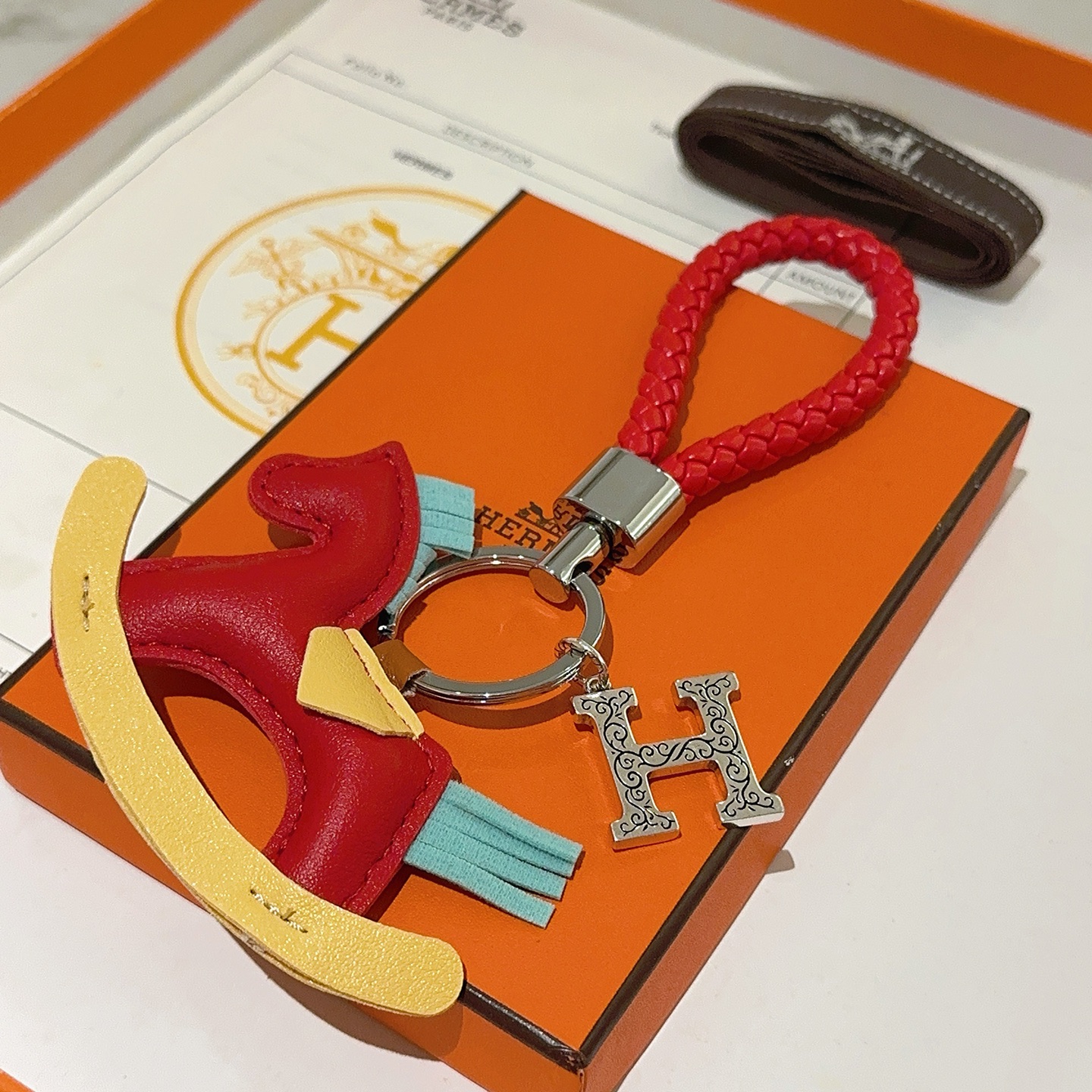 Hermes Rocking Horse H Charm Llavero colgante Cuero trenzado rojo metal plateado cuero multicolor rojo amarillo azul claro Correa trenzada de 10 cm