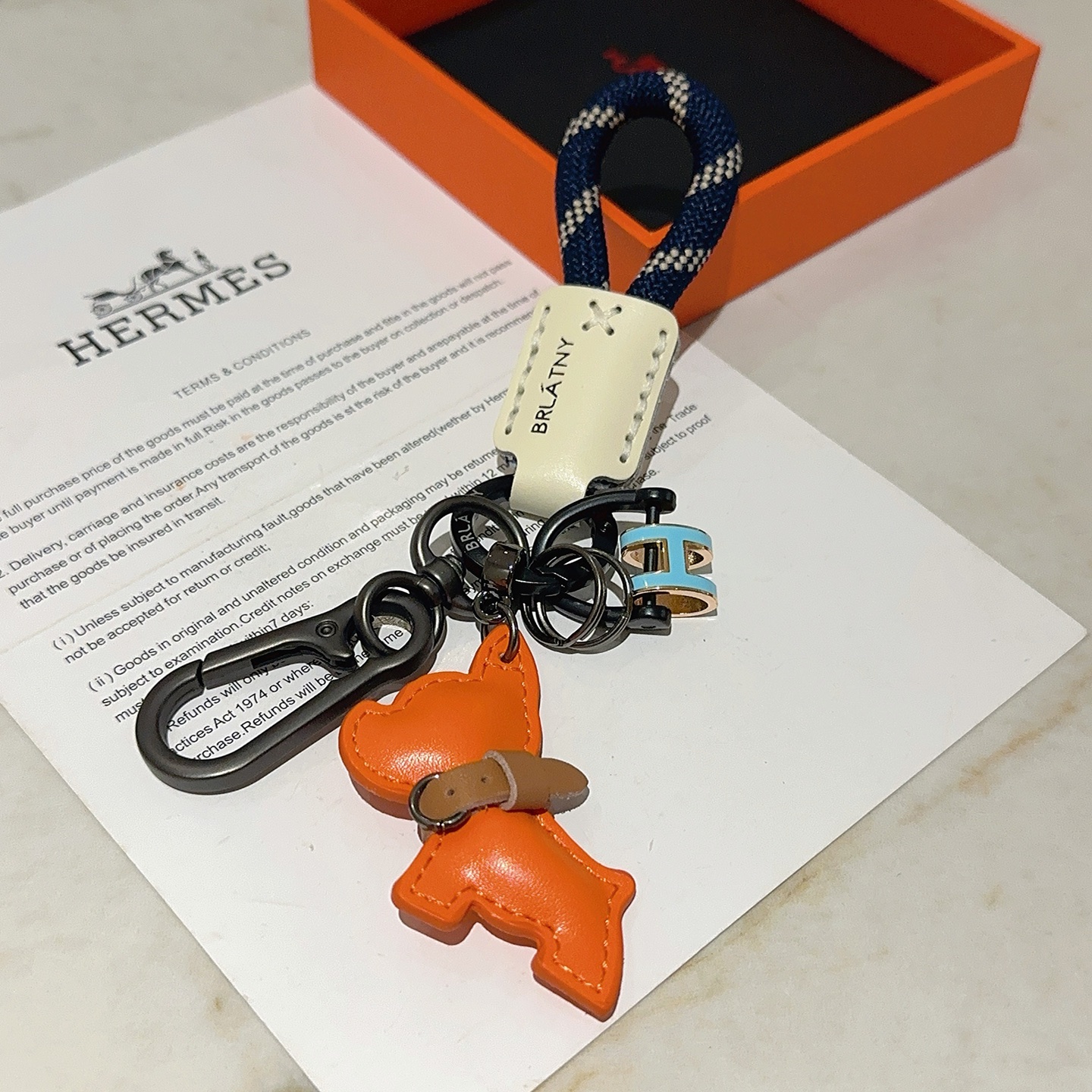 Hermes Pop H Dog Charm Portachiavi Ciondolo Hardware grigio canna di fucile Cavo intrecciato blu navy Accento in pelle color crema Ciondolo per cani in pelle arancione Dettaglio collare in pelle marrone Ciondolo H in smalto azzurro con finiture dorate Lunghezza totale 10 cm