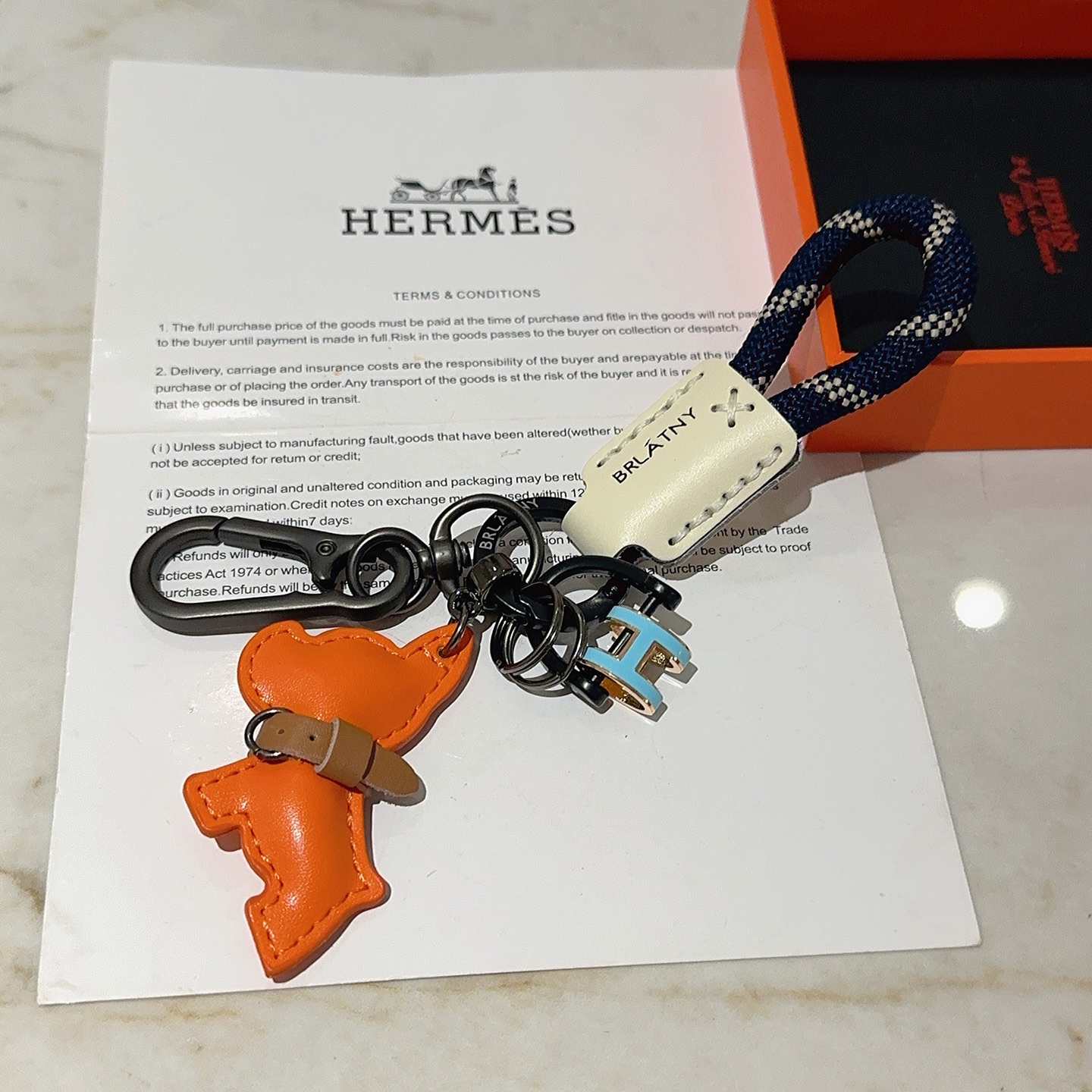 Hermes Pop H Dog Charm Portachiavi Ciondolo Hardware grigio canna di fucile Cavo intrecciato blu navy Accento in pelle color crema Ciondolo per cani in pelle arancione Dettaglio collare in pelle marrone Ciondolo H in smalto azzurro con finiture dorate Lunghezza totale 10 cm