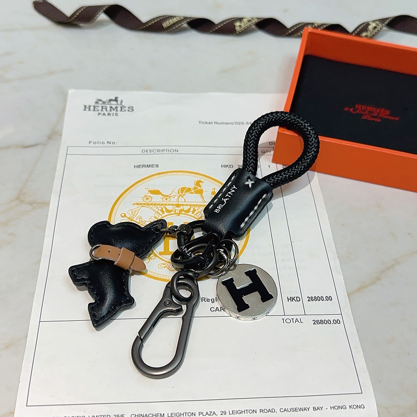 Hermes H Logo Bulldog Charm Chaveiro pingente Cordão trançado preto Couro preto com detalhes em couro bronzeado Hardware em metal prateado com esmalte preto Logotipo H 12 cm de comprimento total