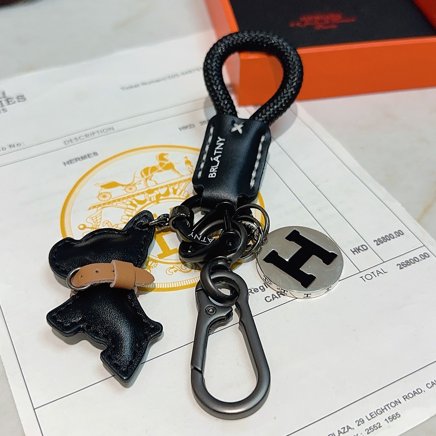 Hermes H Logo Bulldog Charm Chaveiro pingente Cordão trançado preto Couro preto com detalhes em couro bronzeado Hardware em metal prateado com esmalte preto Logotipo H 12 cm de comprimento total