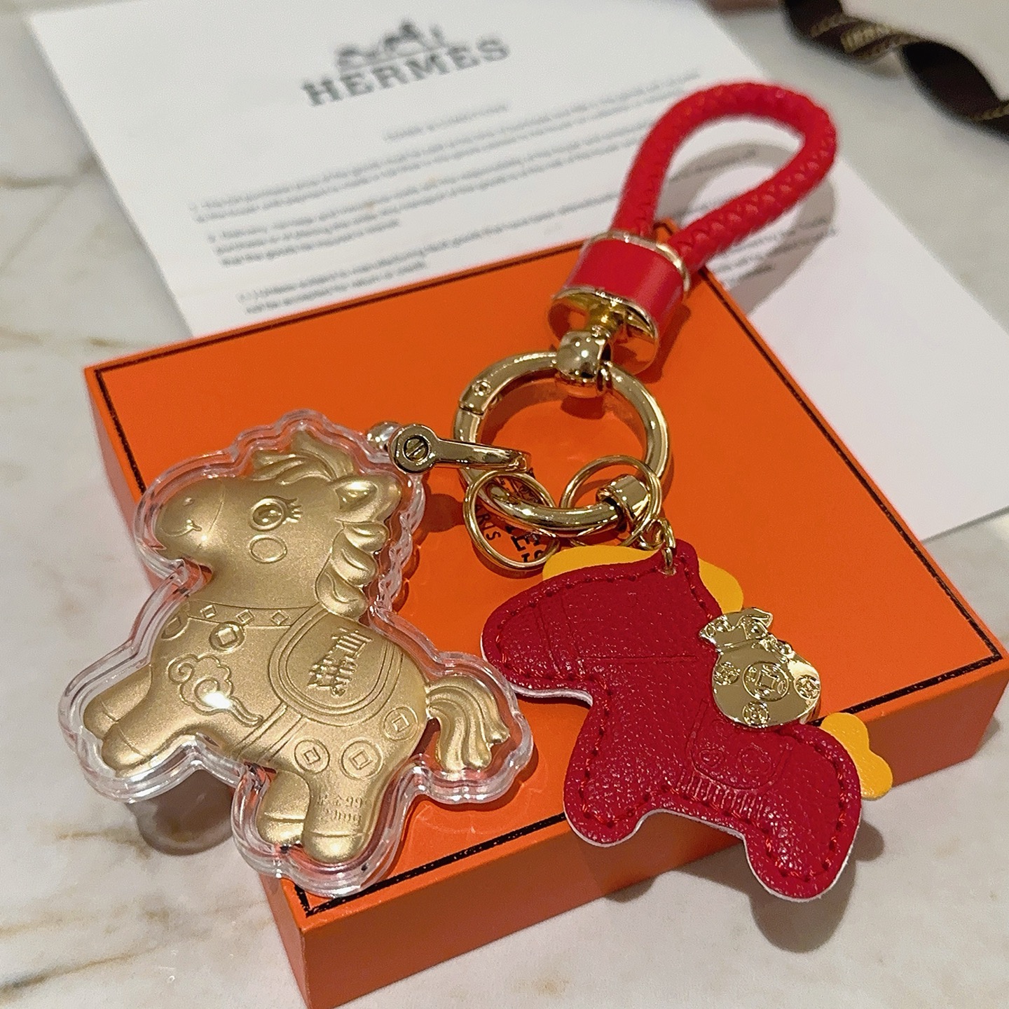 Hermes Lucky Horse Charm Portachiavi Ciondolo Portachiavi in ​​pelle intrecciata rossa in metallo color oro Ciondolo cavallo in pelle rossa Ciondolo cavallo dorato con involucro protettivo trasparente Dettagli accenti gialli Lunghezza totale 10 cm