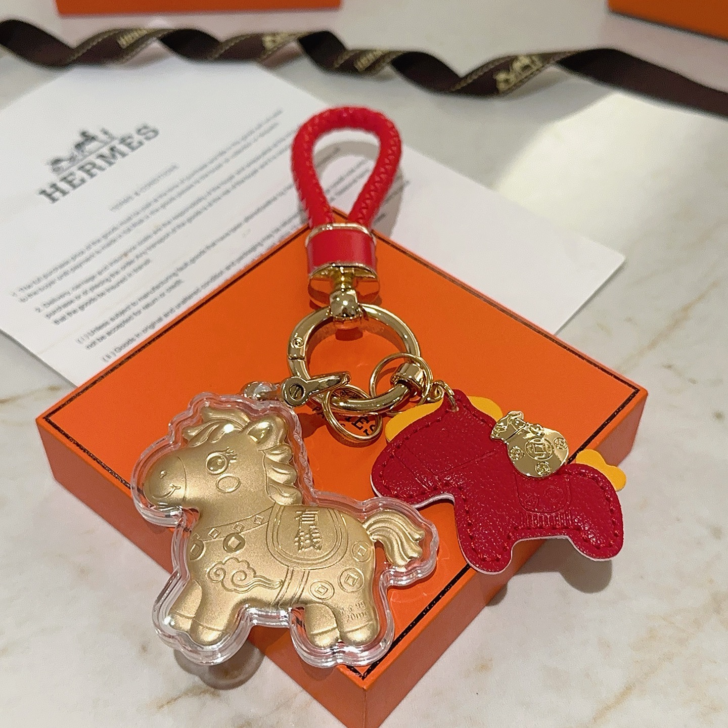 Hermes Lucky Horse Charm Portachiavi Ciondolo Portachiavi in ​​pelle intrecciata rossa in metallo color oro Ciondolo cavallo in pelle rossa Ciondolo cavallo dorato con involucro protettivo trasparente Dettagli accenti gialli Lunghezza totale 10 cm
