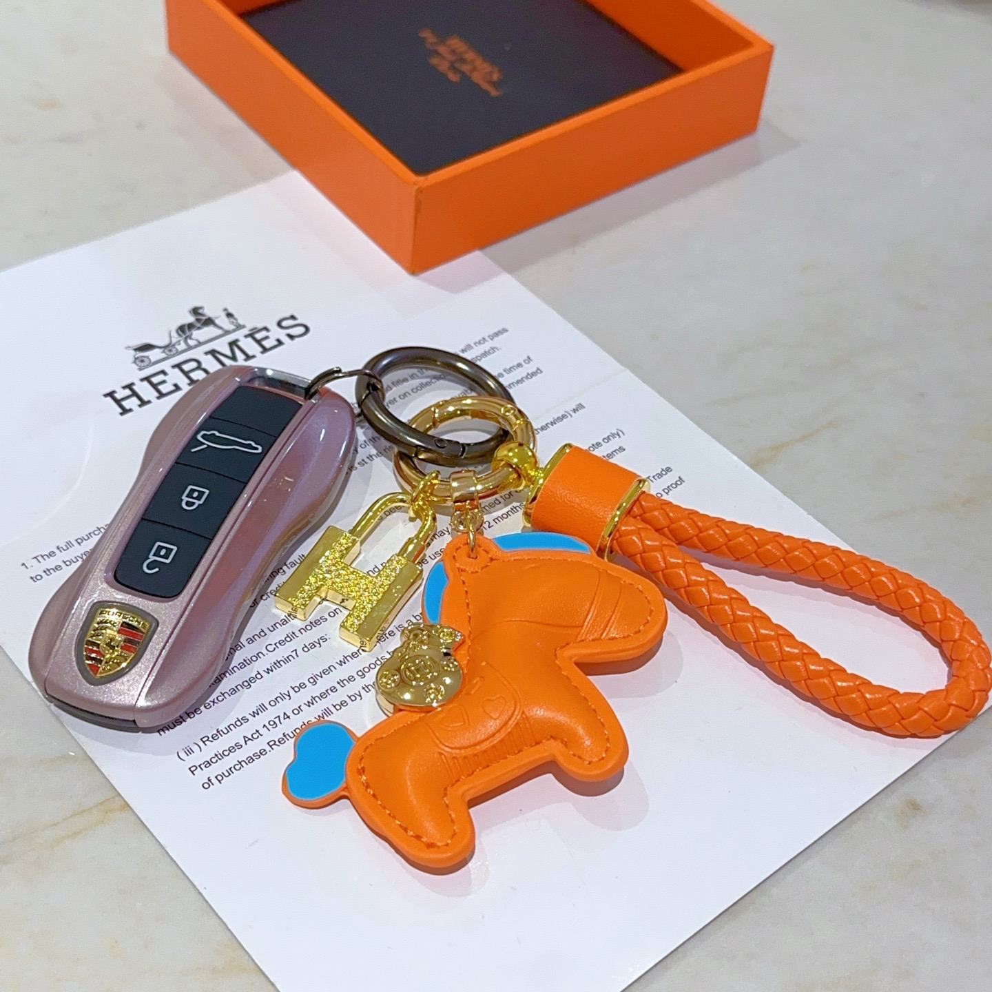 Ciondolo Hermes Rodeo H Lock Key Charm Ciondolo cavallo in pelle arancione intrecciata in pelle intrecciata arancione in metallo color oro con accenti blu, lunghezza totale 10 cm