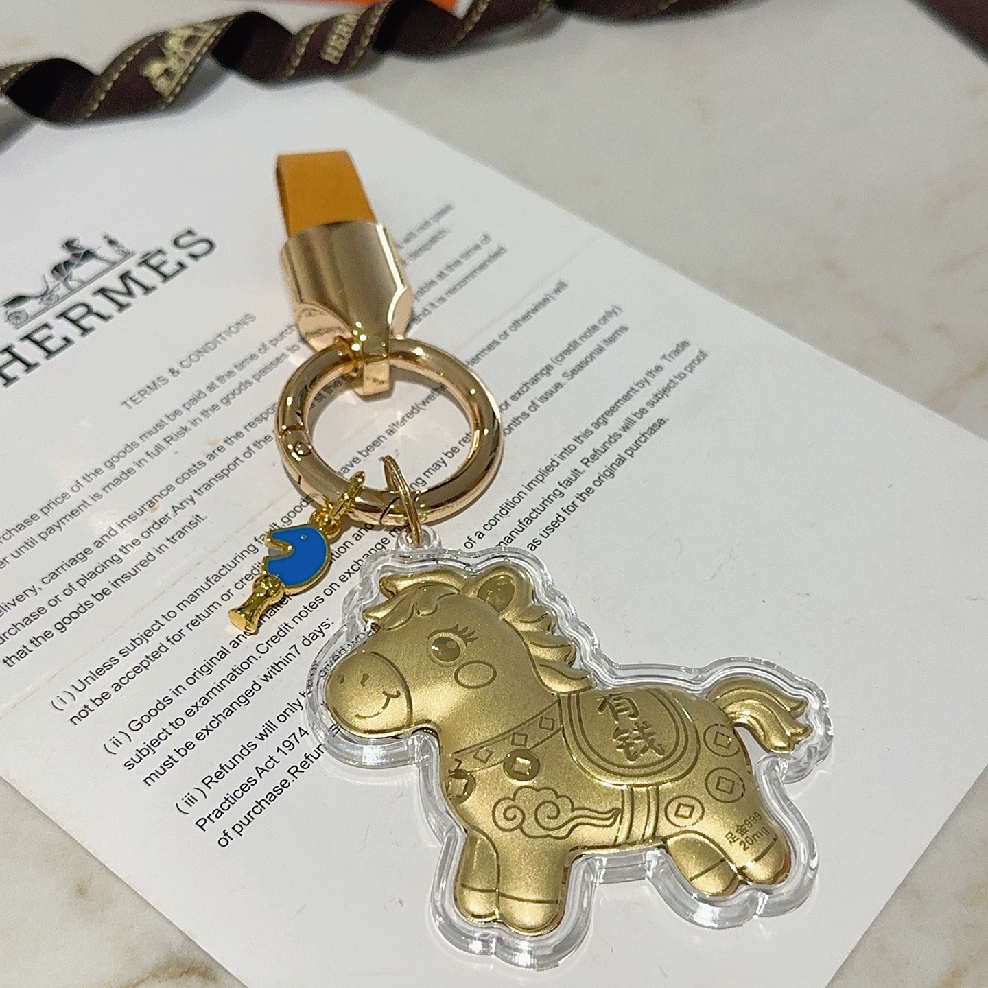 Ciondolo portachiavi Hermes Lucky Horse Charm Metallo color oro con cinturino in pelle arancione accento smaltato blu involucro protettivo trasparente sul ciondolo cavallo dorato Lunghezza totale 9 cm