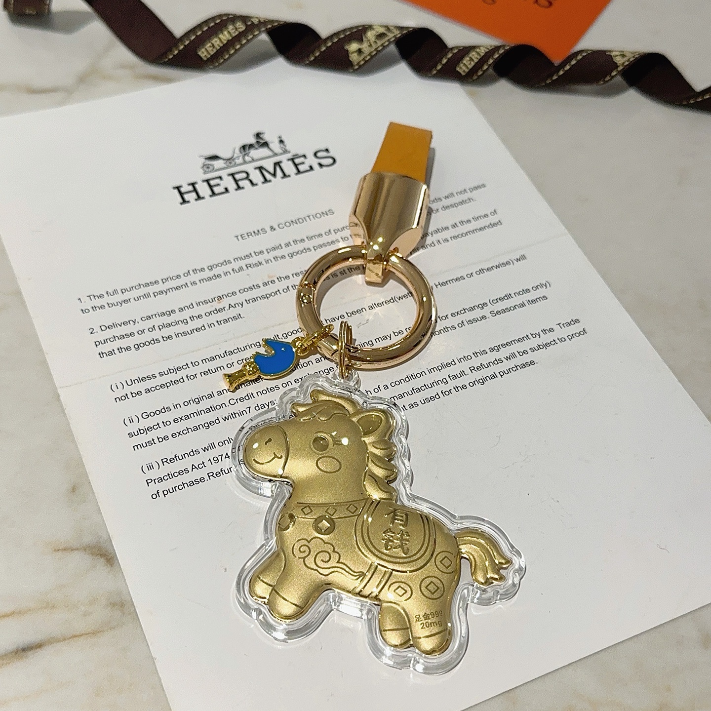 Ciondolo portachiavi Hermes Lucky Horse Charm Metallo color oro con cinturino in pelle arancione accento smaltato blu involucro protettivo trasparente sul ciondolo cavallo dorato Lunghezza totale 9 cm