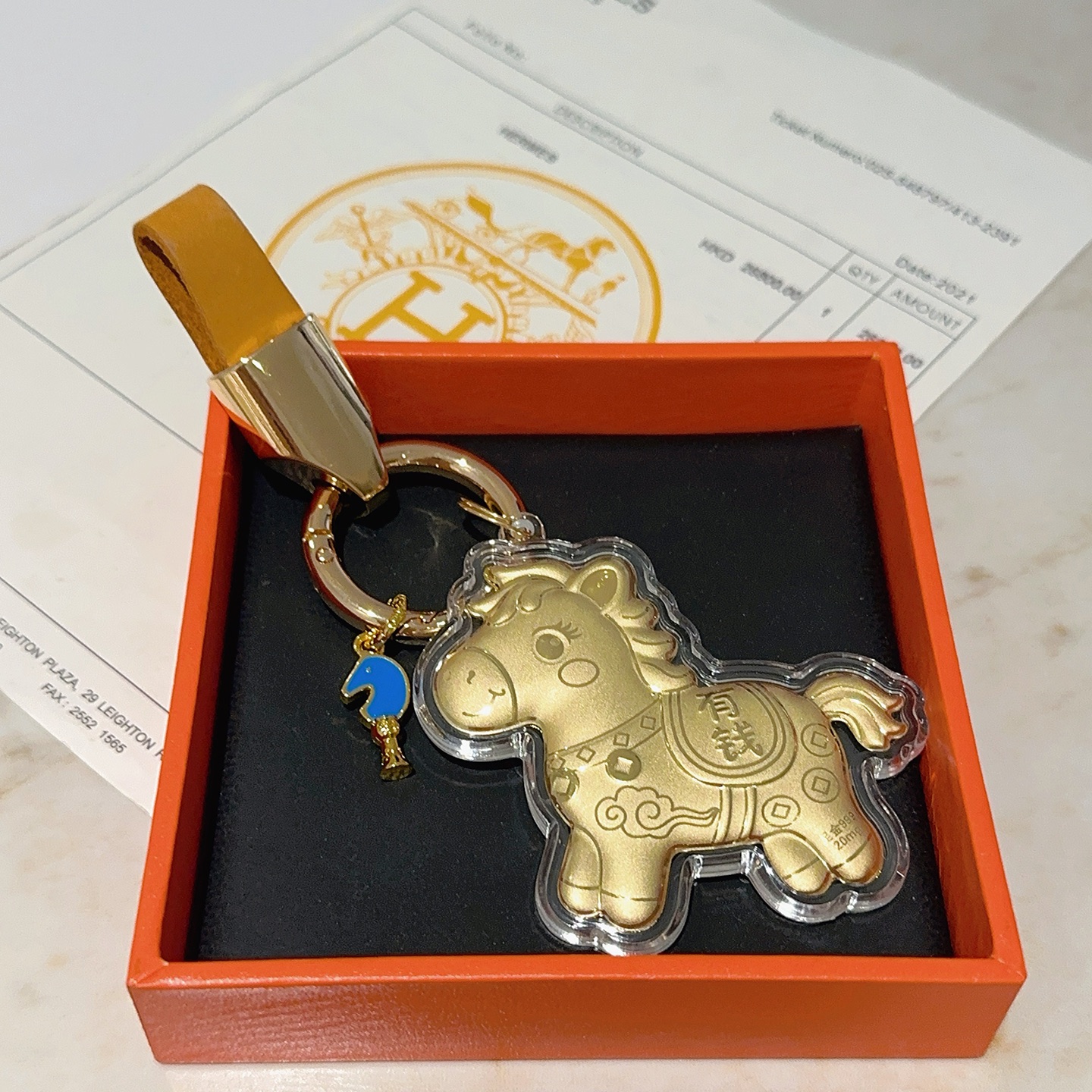Ciondolo portachiavi Hermes Lucky Horse Charm Metallo color oro con cinturino in pelle arancione accento smaltato blu involucro protettivo trasparente sul ciondolo cavallo dorato Lunghezza totale 9 cm