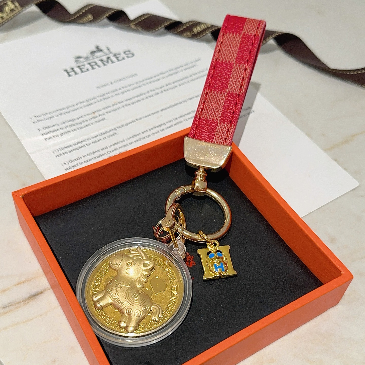 Ciondolo portachiavi Hermes Lucky Horse Fu Charm Cinturino in tela rivestita a scacchi rossi Hardware in metallo color oro Medaglione dorato Ciondolo H in smalto blu Custodia protettiva trasparente con medaglione 10 cm di lunghezza totale