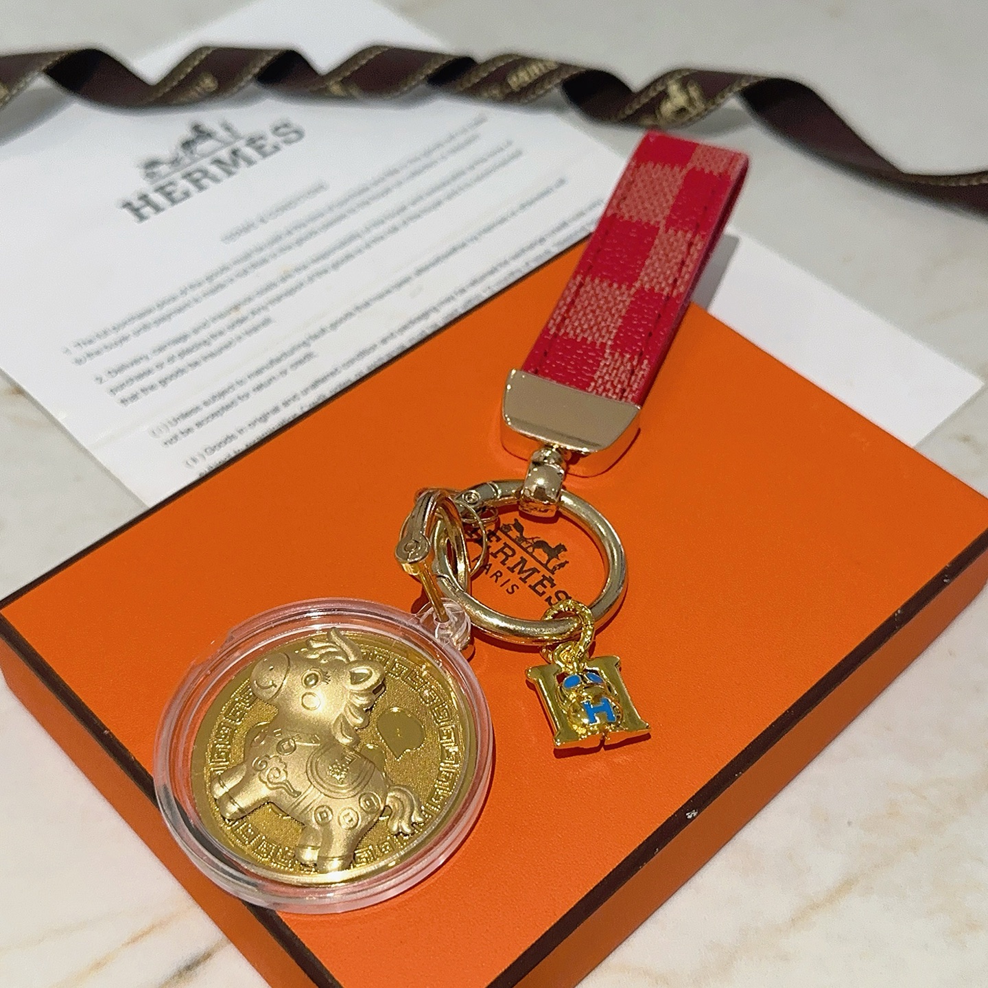 Ciondolo portachiavi Hermes Lucky Horse Fu Charm Cinturino in tela rivestita a scacchi rossi Hardware in metallo color oro Medaglione dorato Ciondolo H in smalto blu Custodia protettiva trasparente con medaglione 10 cm di lunghezza totale