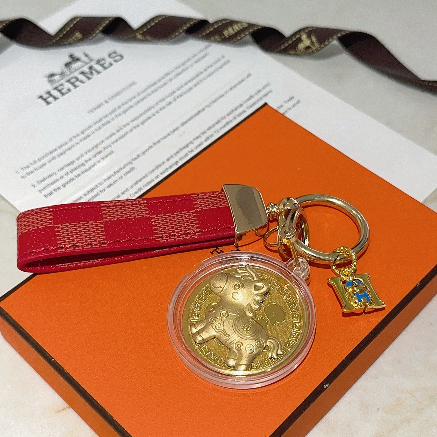 Ciondolo portachiavi Hermes Lucky Horse Fu Charm Cinturino in tela rivestita a scacchi rossi Hardware in metallo color oro Medaglione dorato Ciondolo H in smalto blu Custodia protettiva trasparente con medaglione 10 cm di lunghezza totale