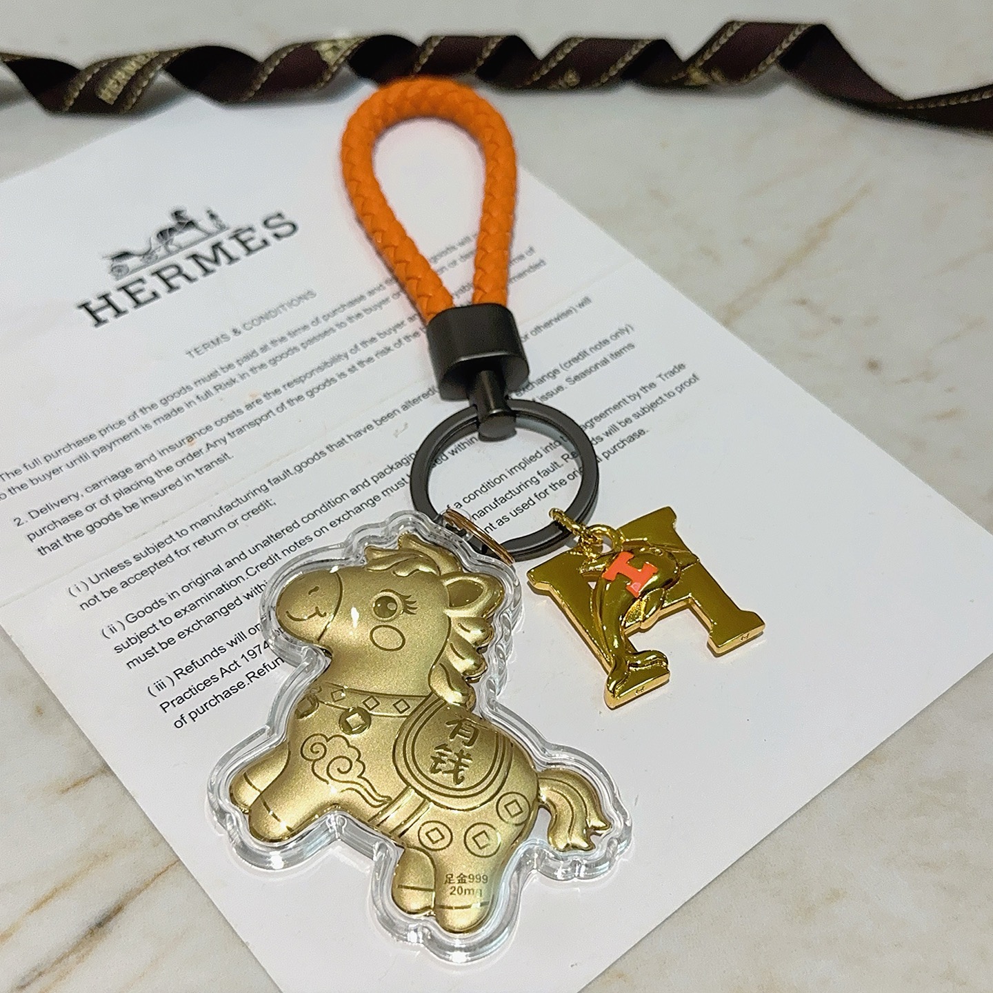 Hermes Lucky Horse H Logo Portachiavi Ciondolo con ciondolo Pelle intrecciata arancione Hardware in canna di fucile Ciondoli in metallo color oro con accento H arancione Rivestimento in acrilico trasparente 10 cm Cinturino intrecciato 4 cm
