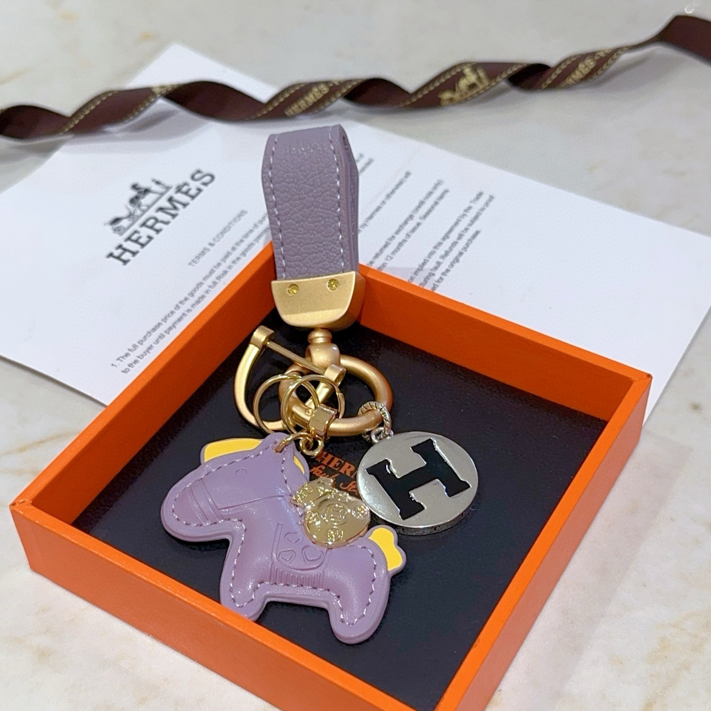 Ciondolo chiave Hermes Rodeo Horse H Logo ciondolo in metallo color oro opaco pelle lavanda accento in pelle gialla metallo argentato con logo H smaltato nero lunghezza totale 10 cm