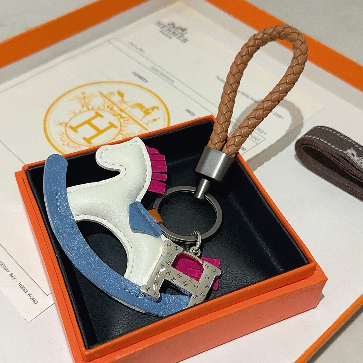 Ciondolo chiave Hermes con cavallo a dondolo H Logo Cinturino in pelle intrecciata marrone Hardware in canna di fucile Ciondolo H color argento Cavallo a dondolo in pelle bianca con sella a bilanciere blu accenti di coda con criniera in pelle fucsia Lunghezza totale 10 cm