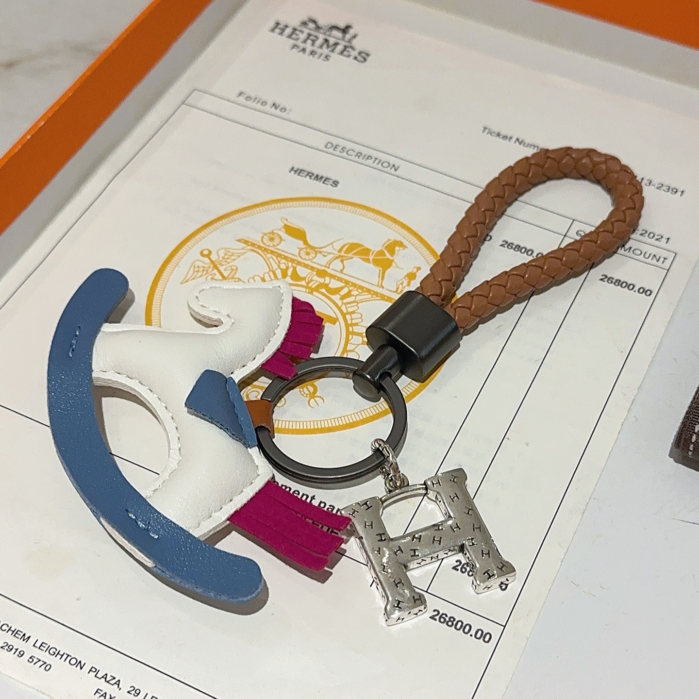 Ciondolo chiave Hermes con cavallo a dondolo H Logo Cinturino in pelle intrecciata marrone Hardware in canna di fucile Ciondolo H color argento Cavallo a dondolo in pelle bianca con sella a bilanciere blu accenti di coda con criniera in pelle fucsia Lunghezza totale 10 cm