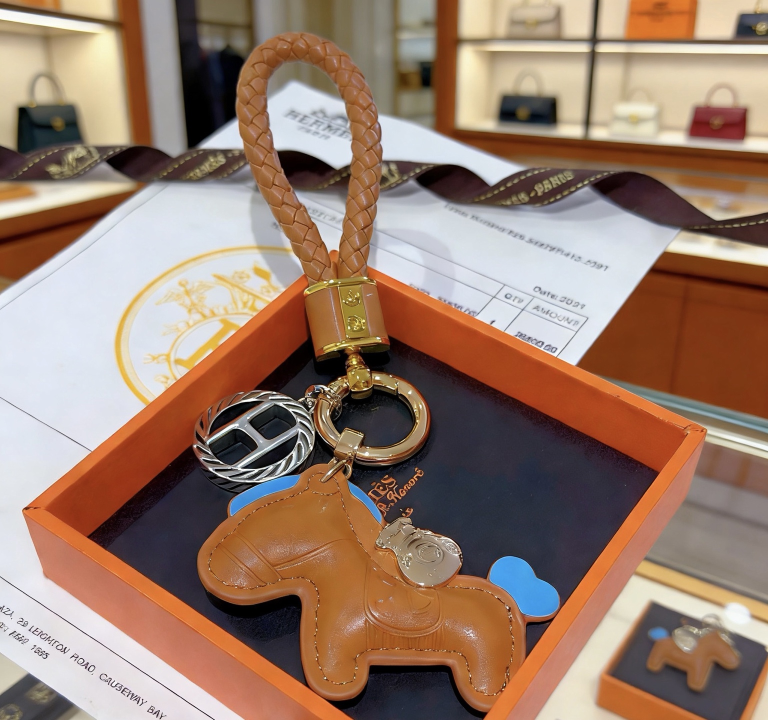 Ciondolo con chiave Hermes Rodeo con cinturino intrecciato Pelle marrone oro con accenti celesti Hardware in metallo color oro e argento Lunghezza totale 12 cm