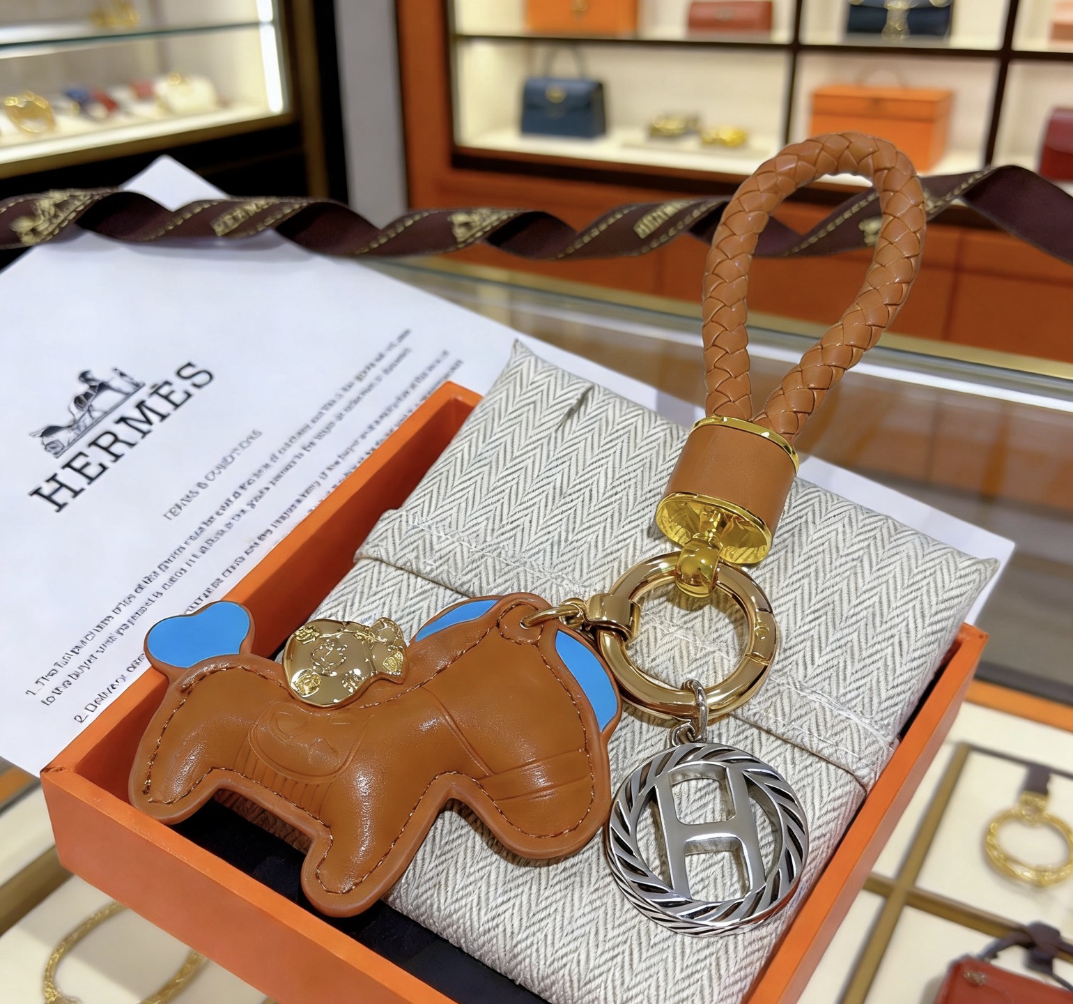 Ciondolo con chiave Hermes Rodeo con cinturino intrecciato Pelle marrone oro con accenti celesti Hardware in metallo color oro e argento Lunghezza totale 12 cm