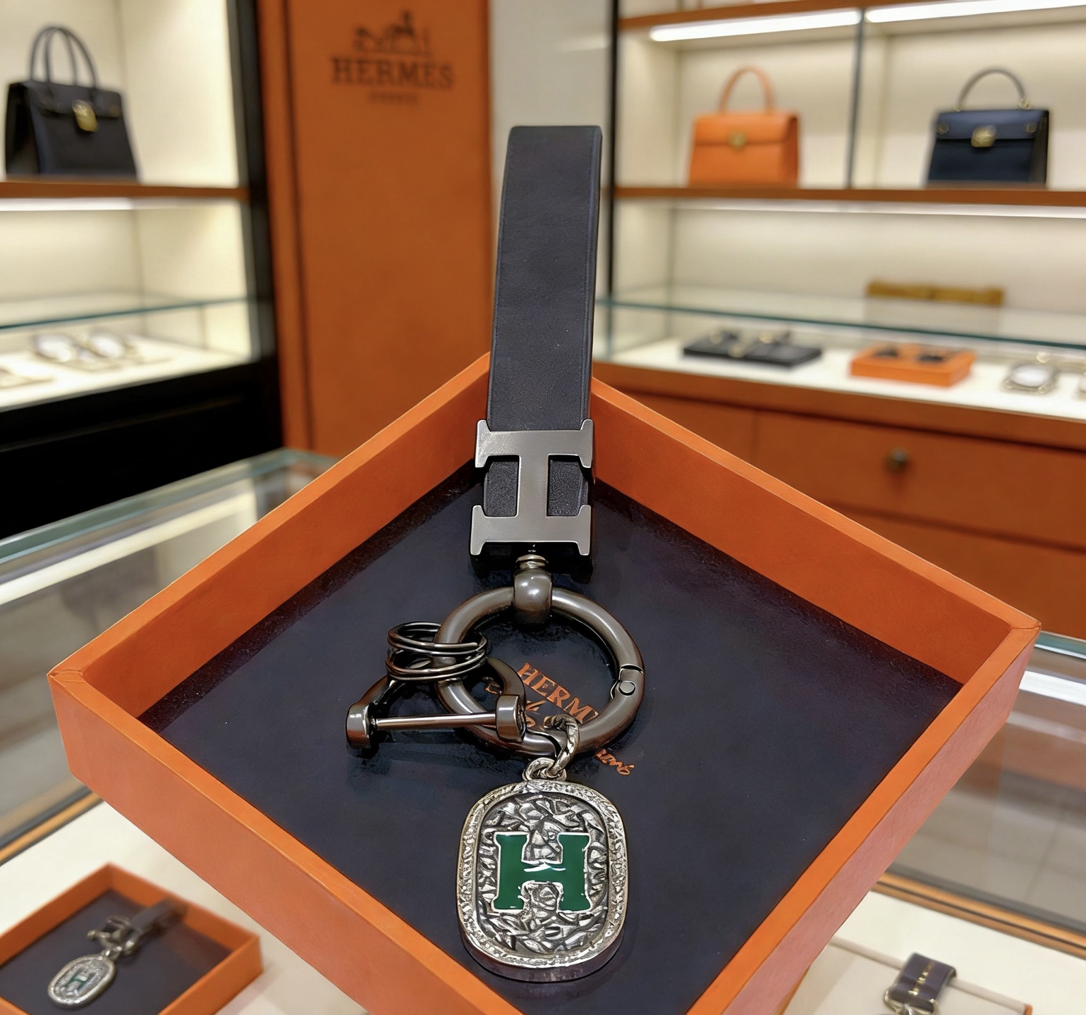Ciondolo con chiave in pelle con logo Hermes H. Dettaglio H in metallo grigio canna di fucile, pelle nera, smalto verde. Lunghezza cinturino 10 cm
