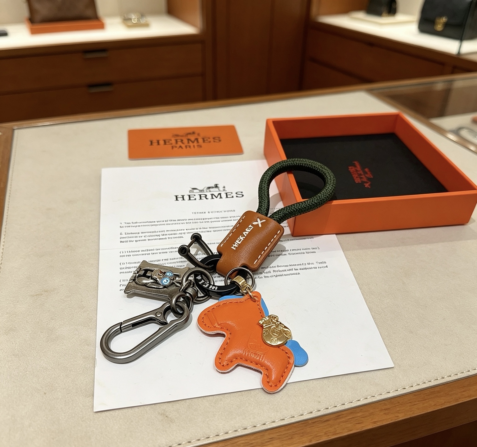 Ciondolo portachiavi Hermes Rodeo Horse Charm Pelle arancione con accenti blu pelle marrone cordone intrecciato verde scuro hardware canna di fucile ciondolo in metallo color oro ciondolo H color argento con dettagli in smalto blu lunghezza totale 12 cm