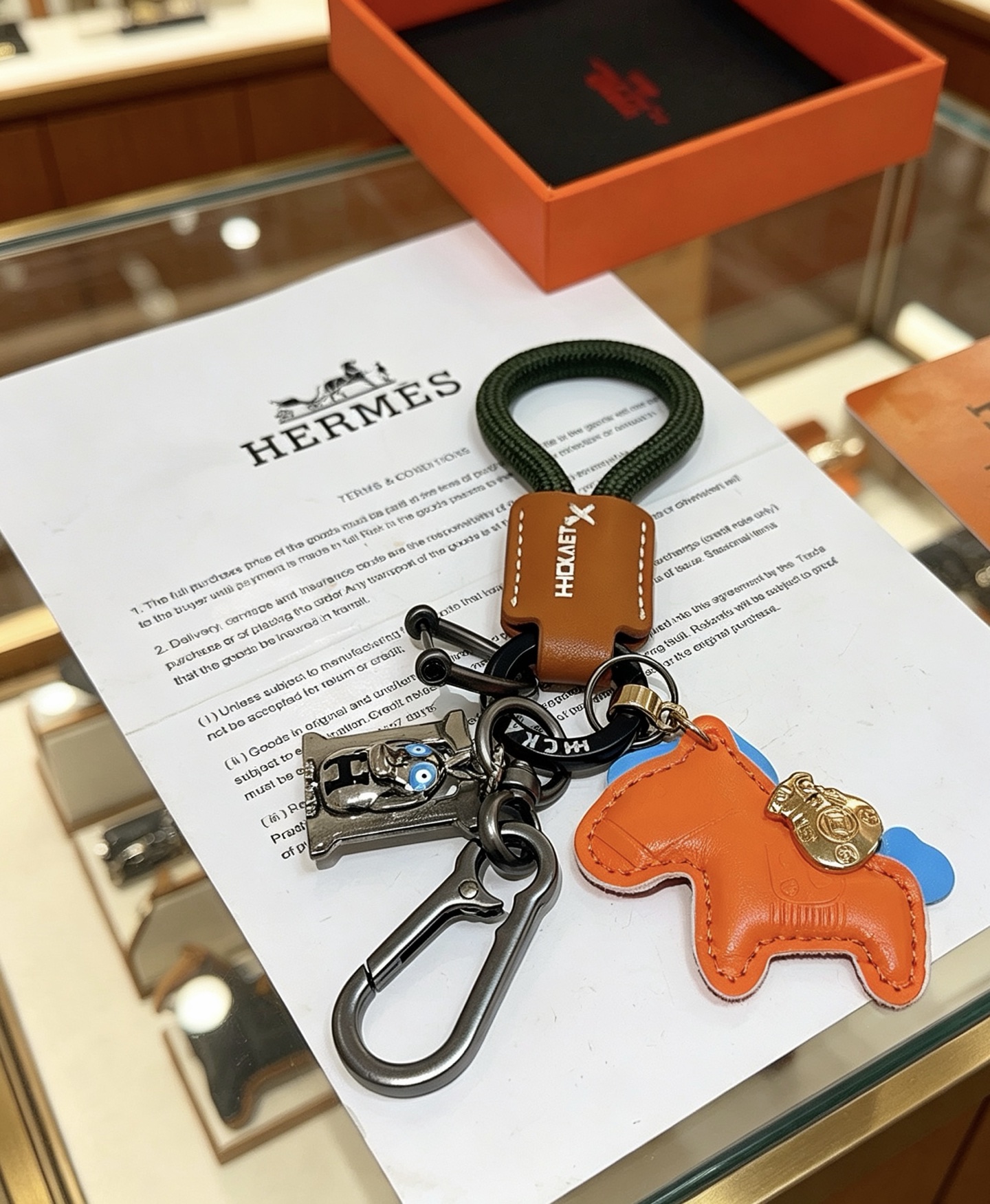 Ciondolo portachiavi Hermes Rodeo Horse Charm Pelle arancione con accenti blu pelle marrone cordone intrecciato verde scuro hardware canna di fucile ciondolo in metallo color oro ciondolo H color argento con dettagli in smalto blu lunghezza totale 12 cm