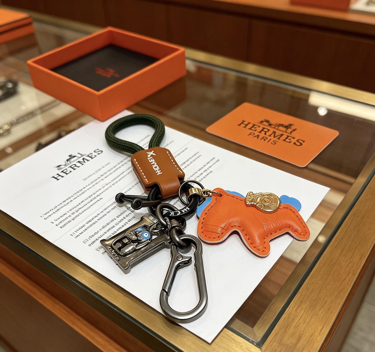 Ciondolo portachiavi Hermes Rodeo Horse Charm Pelle arancione con accenti blu pelle marrone cordone intrecciato verde scuro hardware canna di fucile ciondolo in metallo color oro ciondolo H color argento con dettagli in smalto blu lunghezza totale 12 cm