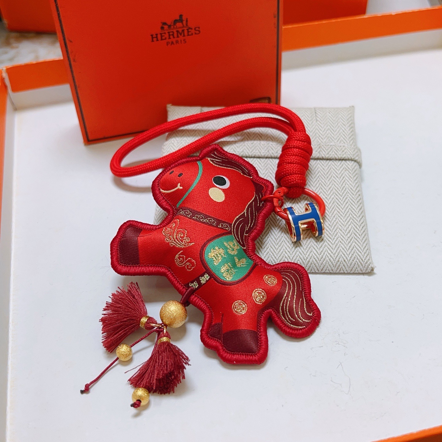 Ciondolo Hermes Chinese New Year Horse Charm Tessuto rosso con accenti dorati smalto blu H hardware verde dettaglio sella nappe bordeaux lunghezza cinturino 12 cm