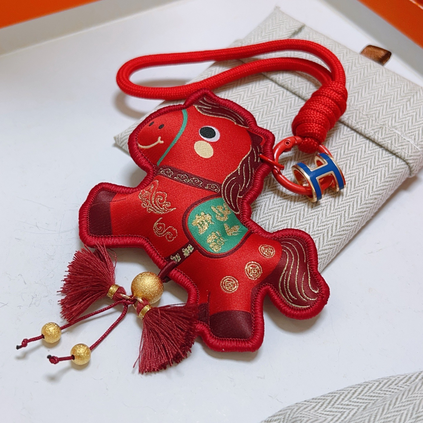 Ciondolo Hermes Chinese New Year Horse Charm Tessuto rosso con accenti dorati smalto blu H hardware verde dettaglio sella nappe bordeaux lunghezza cinturino 12 cm