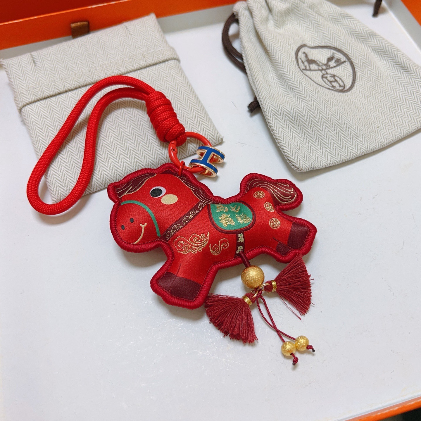 Ciondolo Hermes Chinese New Year Horse Charm Tessuto rosso con accenti dorati smalto blu H hardware verde dettaglio sella nappe bordeaux lunghezza cinturino 12 cm