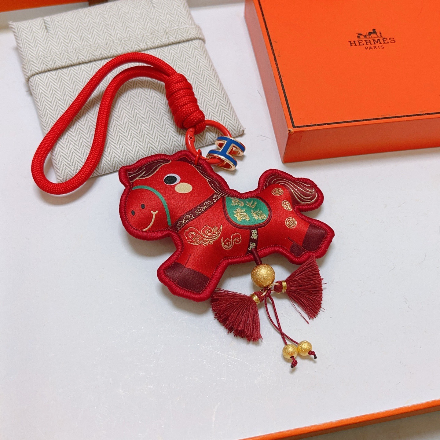 Ciondolo Hermes Chinese New Year Horse Charm Tessuto rosso con accenti dorati smalto blu H hardware verde dettaglio sella nappe bordeaux lunghezza cinturino 12 cm