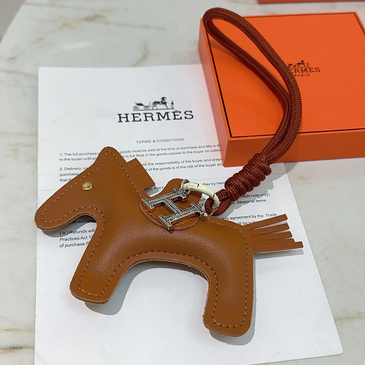 Ciondolo per borsa Hermes Rodeo Pegase Horse con pendente in cristallo H. Pelle marrone oro, metallo color argento con pavé di cristalli trasparenti, hardware bianco sporco, cordone marrone terracotta, lunghezza totale del ciondolo: 8 cm.