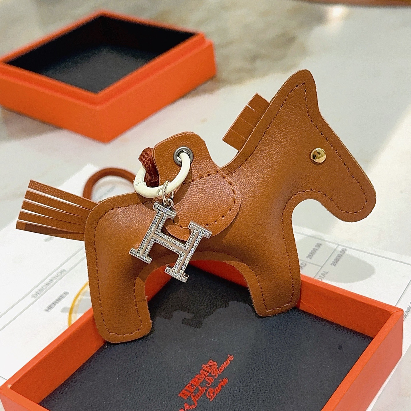 Ciondolo per borsa Hermes Rodeo Pegase Horse con pendente in cristallo H. Pelle marrone oro, metallo color argento con pavé di cristalli trasparenti, hardware bianco sporco, cordone marrone terracotta, lunghezza totale del ciondolo: 8 cm.