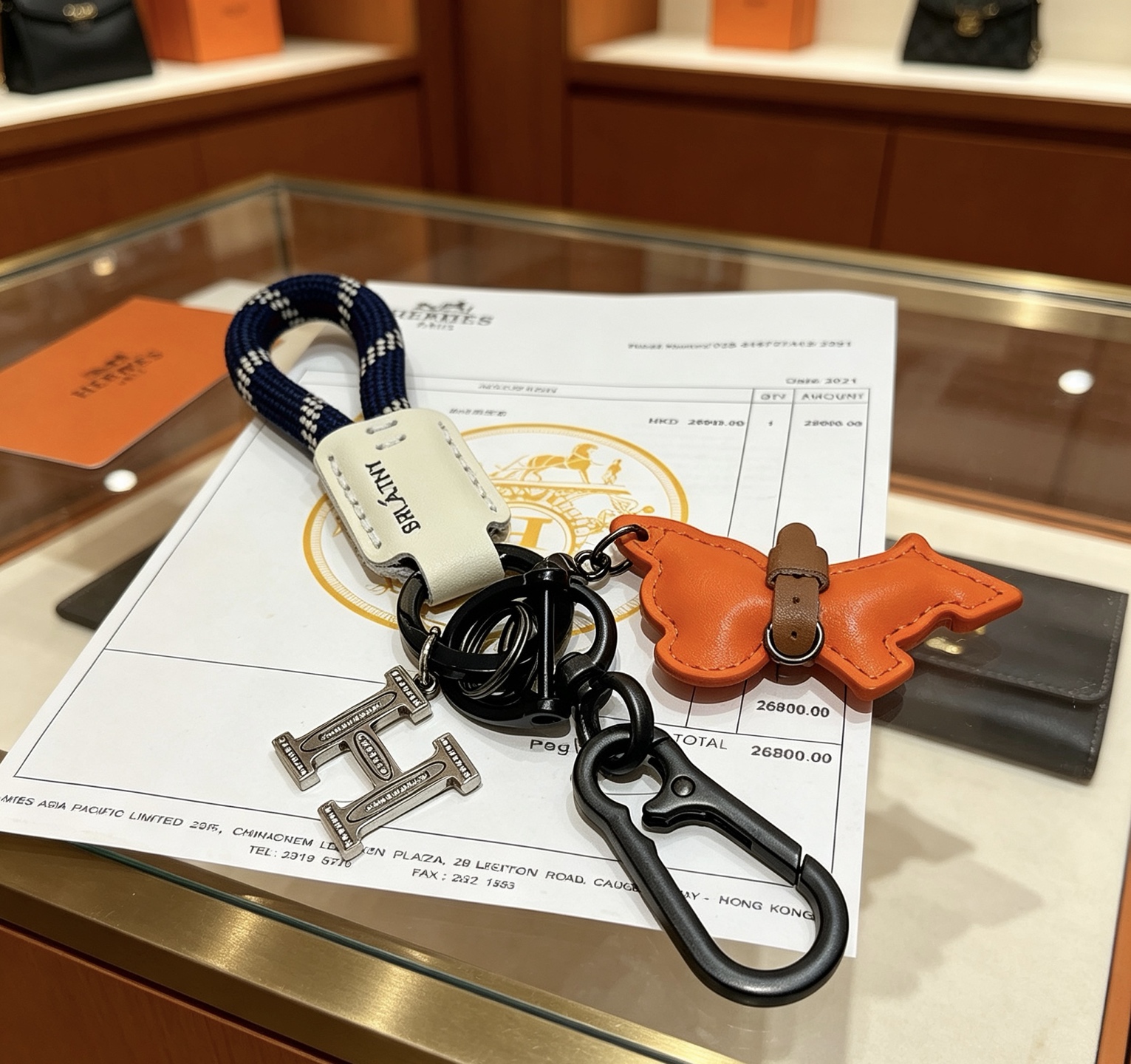 Hermes H Logo Puppy Charm Llavero colgante Herrajes de bronce de cañón Charm de cachorro de cuero naranja Etiqueta de cuero crema Correa tejida azul marino con patrón de cuadros blancos Detalle de collar de cuero marrón 12 cm de longitud total