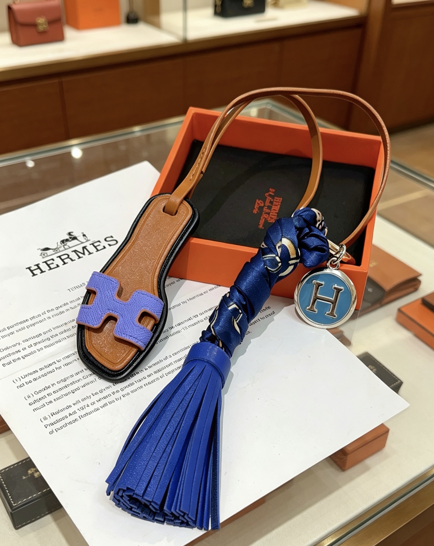 Hermes Oran Sandalia Borla Bolso Charm Llavero colgante Cuero marrón Púrpura H Detalle de sandalia Borla de cuero azul real Envoltura de seda azul marino Metal plateado con esmalte azul H Charm 12 cm de longitud total