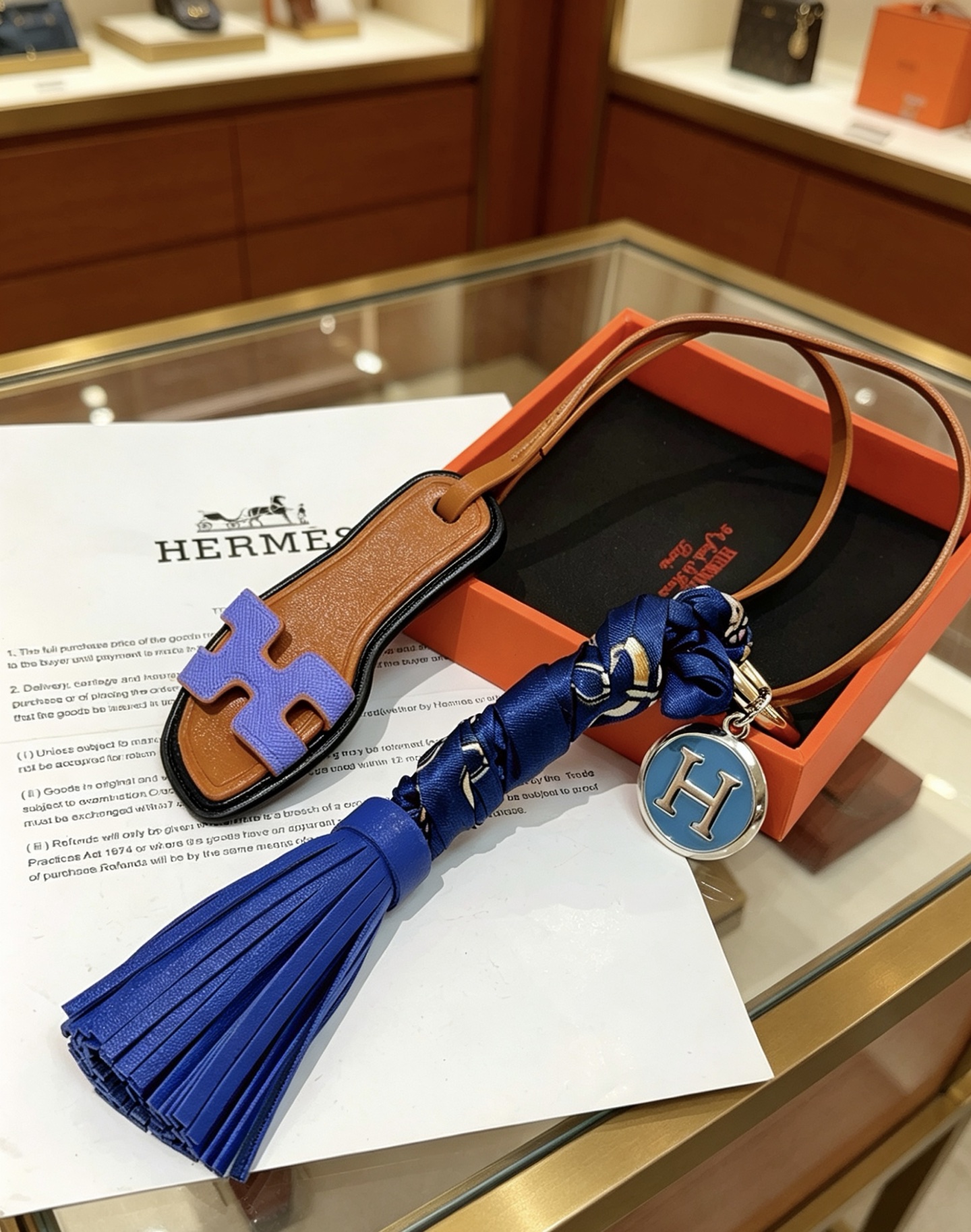 Hermes Oran Sandalia Borla Bolso Charm Llavero colgante Cuero marrón Púrpura H Detalle de sandalia Borla de cuero azul real Envoltura de seda azul marino Metal plateado con esmalte azul H Charm 12 cm de longitud total