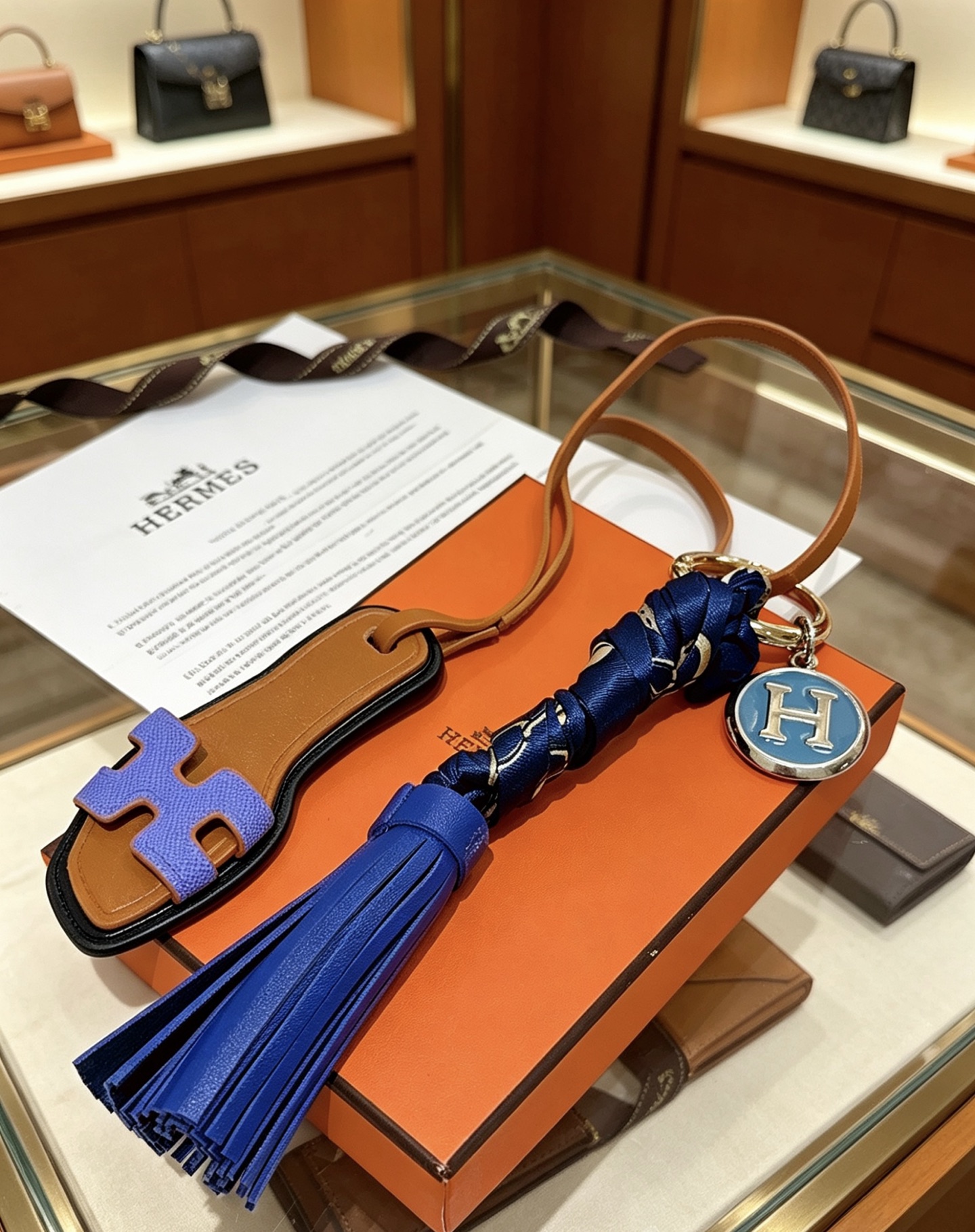Hermes Oran Sandalia Borla Bolso Charm Llavero colgante Cuero marrón Púrpura H Detalle de sandalia Borla de cuero azul real Envoltura de seda azul marino Metal plateado con esmalte azul H Charm 12 cm de longitud total