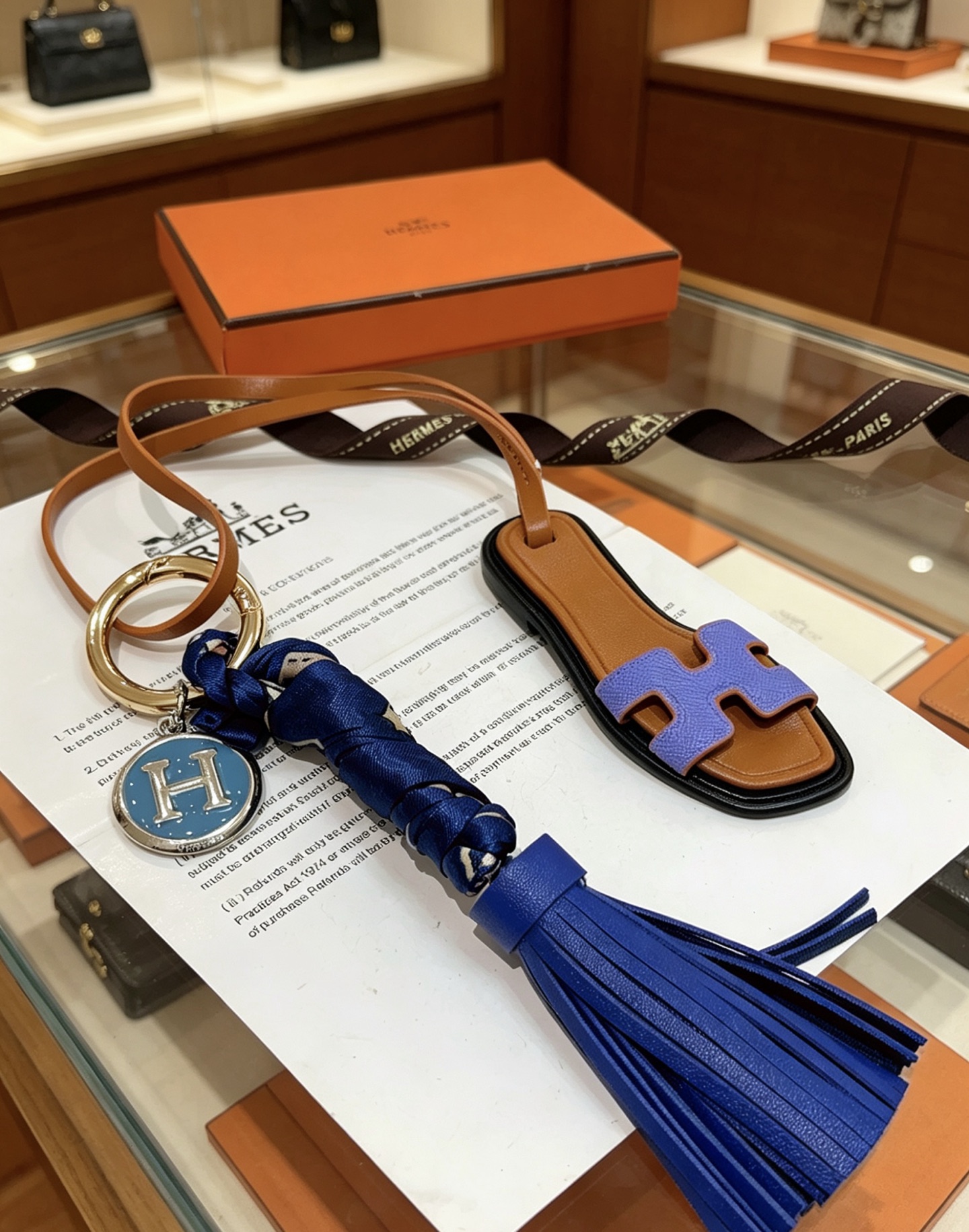 Hermes Oran Sandalia Borla Bolso Charm Llavero colgante Cuero marrón Púrpura H Detalle de sandalia Borla de cuero azul real Envoltura de seda azul marino Metal plateado con esmalte azul H Charm 12 cm de longitud total