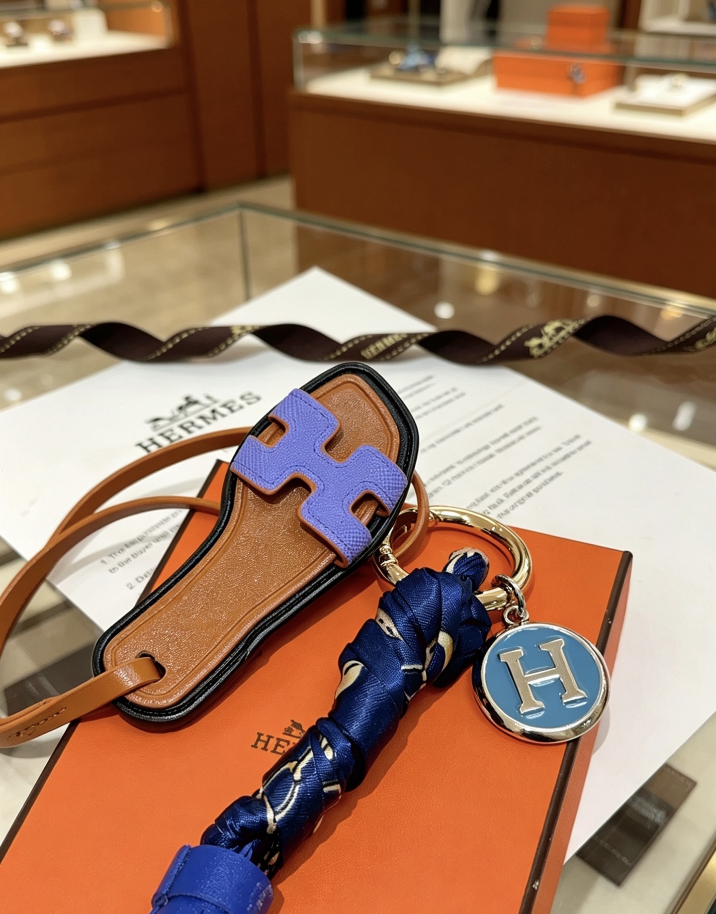 Hermes Oran Sandalia Borla Bolso Charm Llavero colgante Cuero marrón Púrpura H Detalle de sandalia Borla de cuero azul real Envoltura de seda azul marino Metal plateado con esmalte azul H Charm 12 cm de longitud total