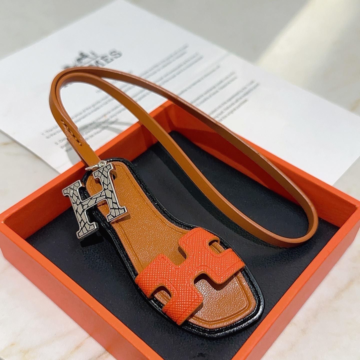 Hermes Oran Sandal Bag Charm colgante Metal plateado naranja Cuero Epsom dorado Cuero Swift ribete de borde negro Longitud de la correa de 17 cm