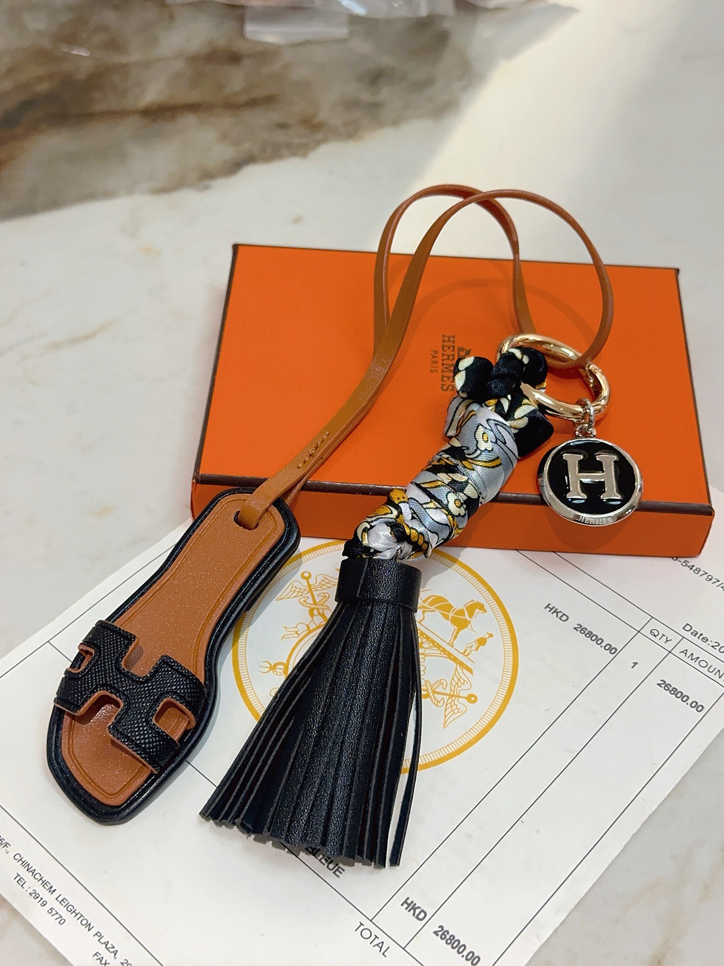 Hermes Oran Sandal Tassel H Logo Keychain Charm pingente metal dourado couro preto couro bronzeado metal prateado com esmalte preto seda cinza com estampa floral dourada e preta 12 cm de comprimento total
