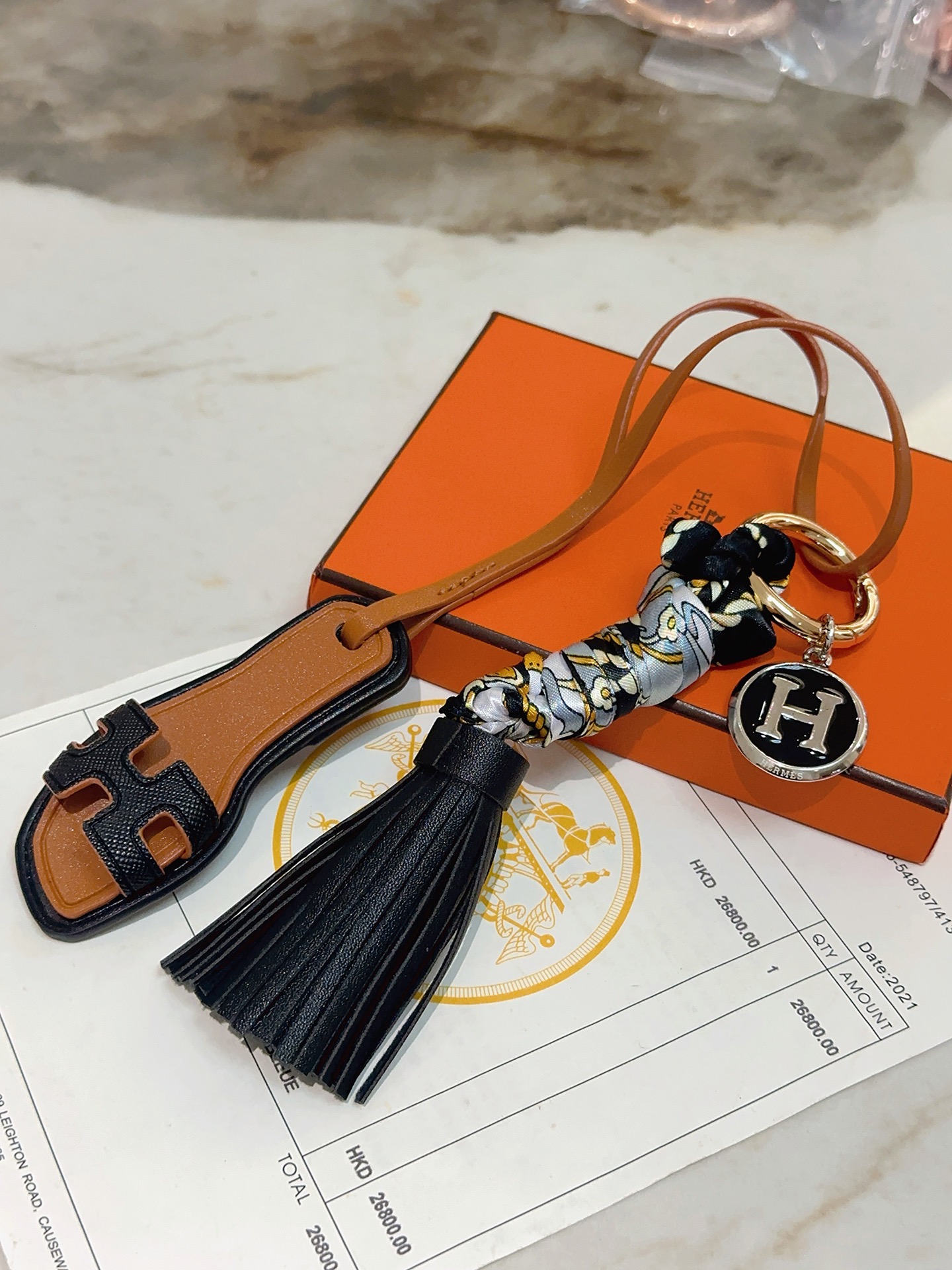 Hermes Oran Sandal Tassel H Logo Keychain Charm pingente metal dourado couro preto couro bronzeado metal prateado com esmalte preto seda cinza com estampa floral dourada e preta 12 cm de comprimento total