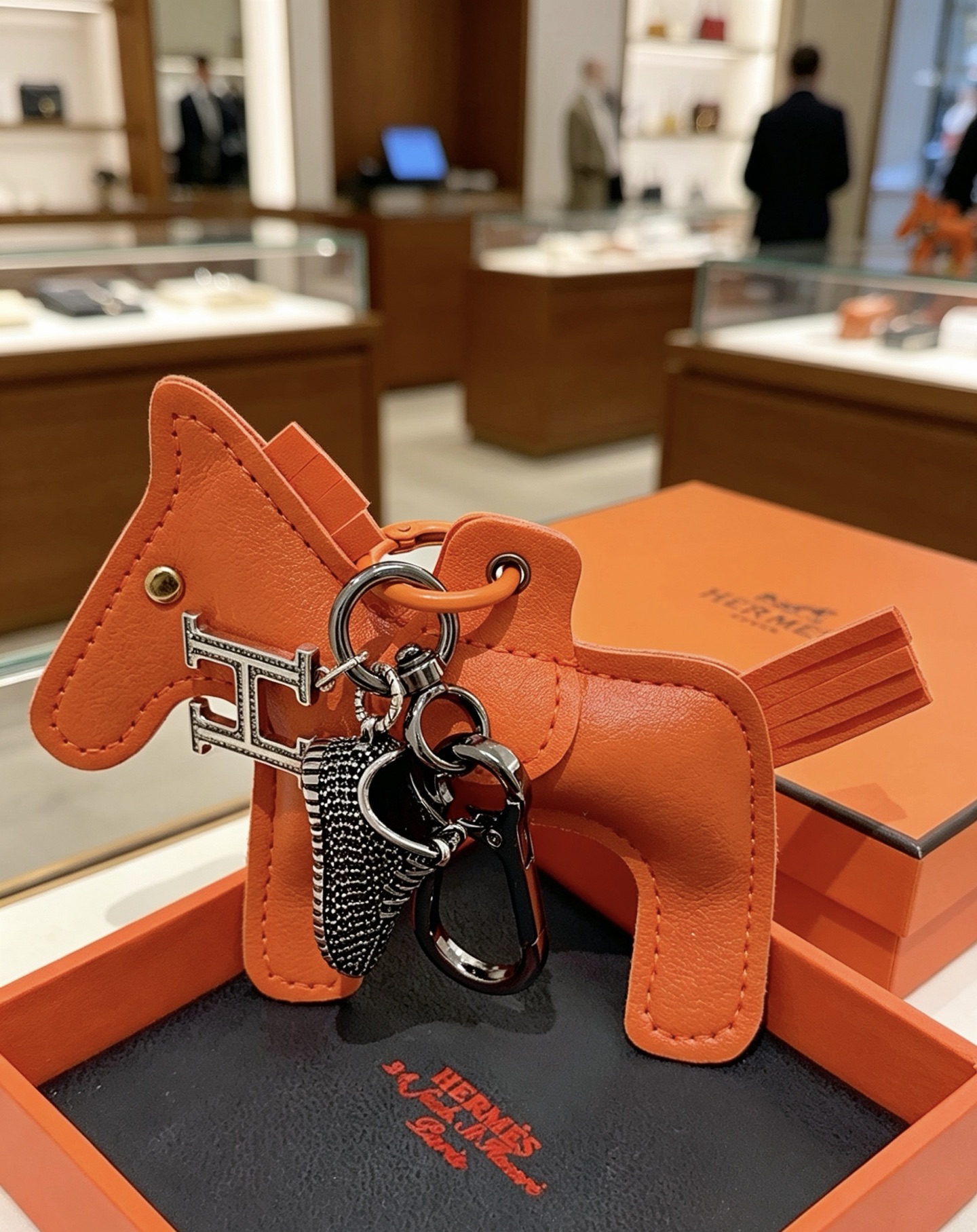Hermes Rodeo H Logo Sneaker Charm Llavero colgante Herrajes de cuero naranja detalles en cristal transparente Charm de zapatilla en negro y plata 12 cm de longitud total