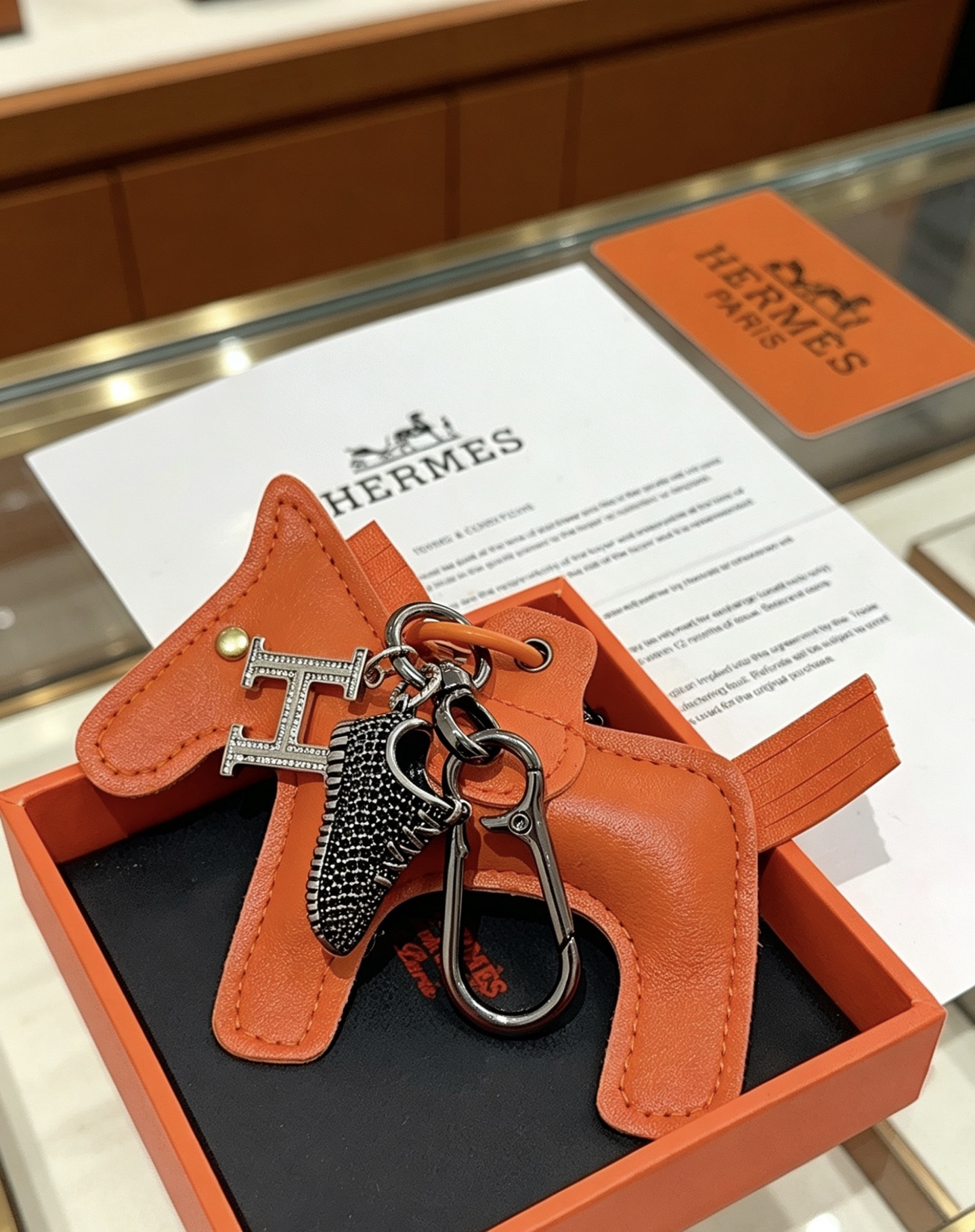 Hermes Rodeo H Logo Sneaker Charm Llavero colgante Herrajes de cuero naranja detalles en cristal transparente Charm de zapatilla en negro y plata 12 cm de longitud total