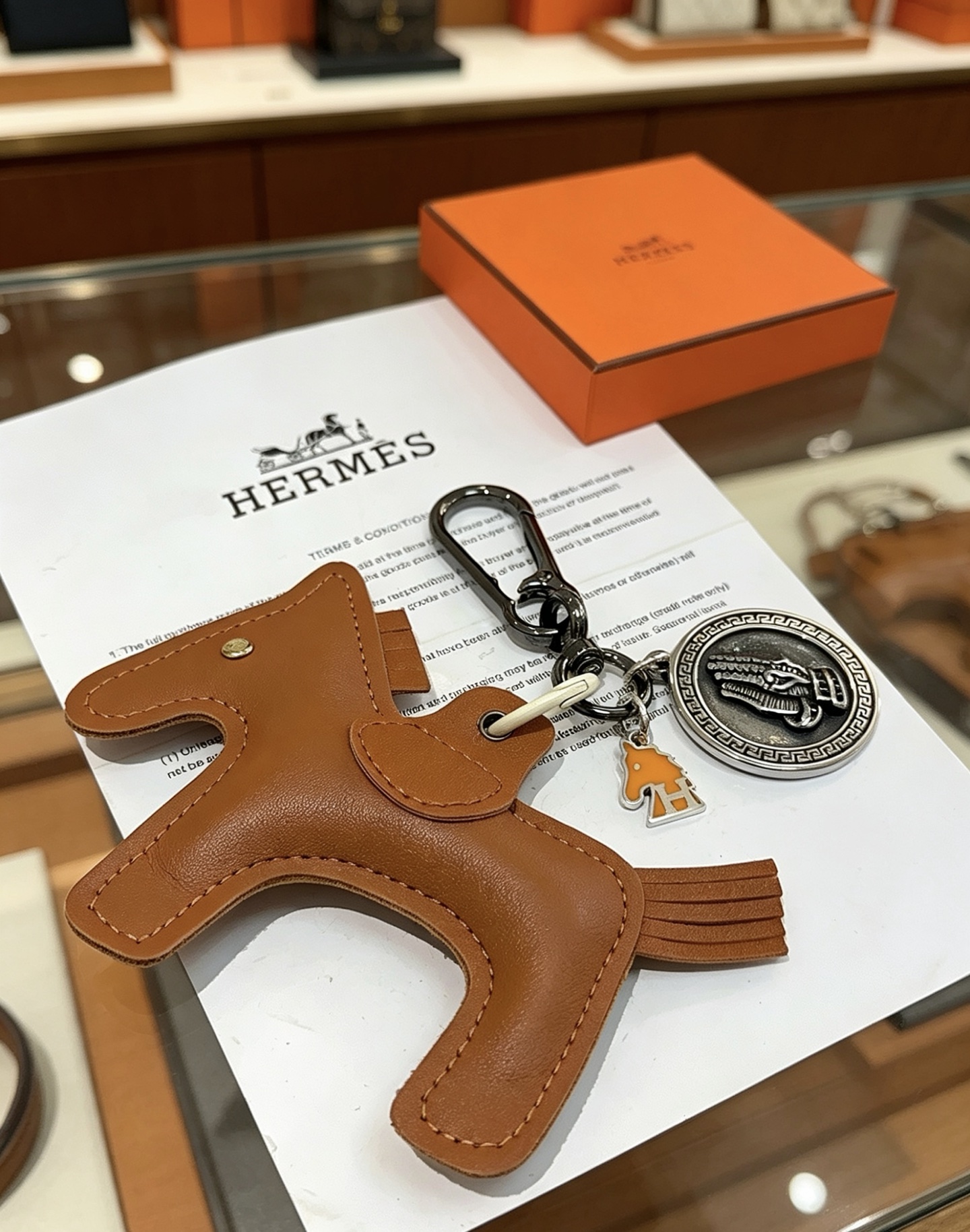Ciondolo Hermes Cheval con chiave a cavallo, in pelle marrone oro, metallo color argento antico, smalto arancione, lunghezza totale 10 cm