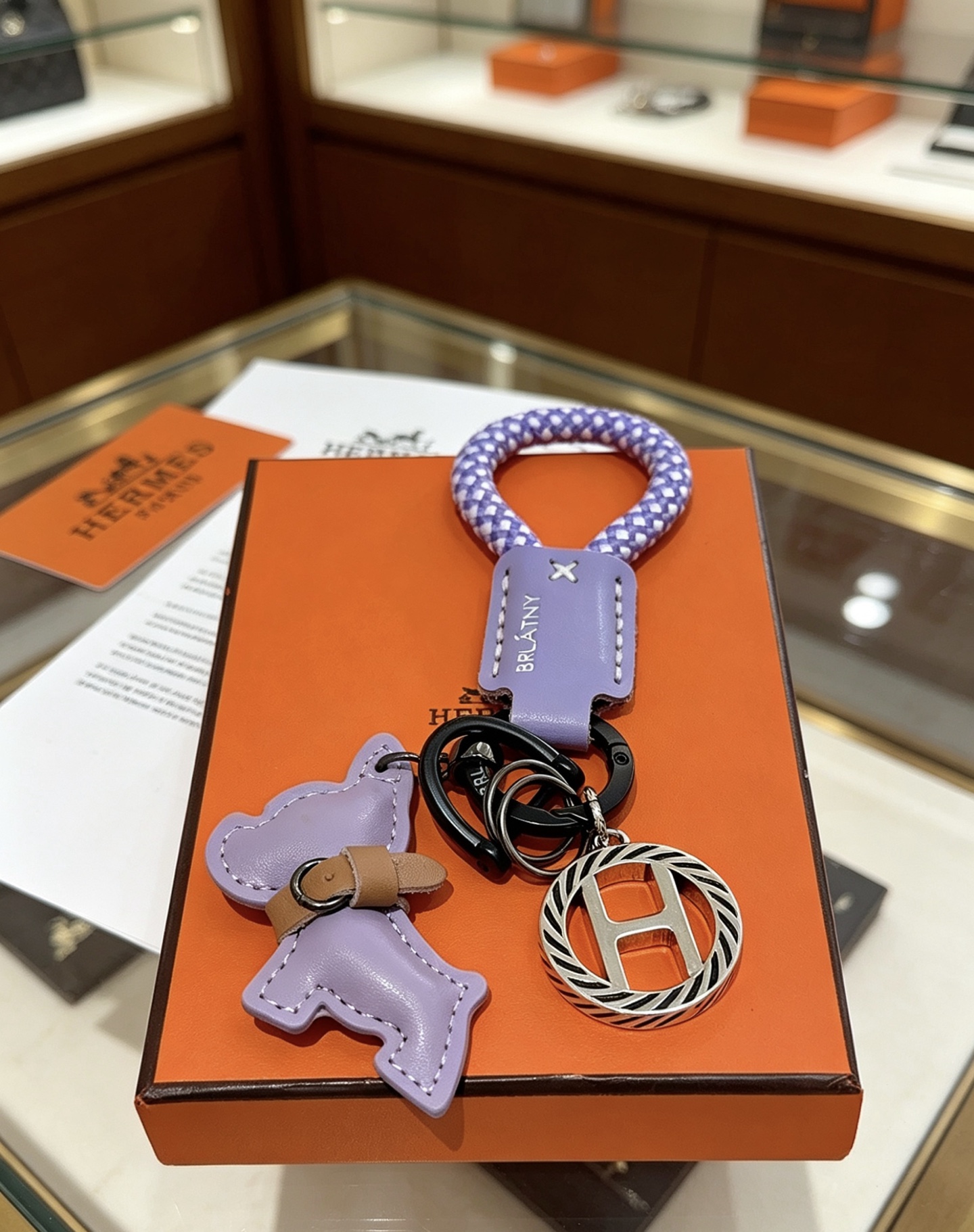 Hermes Rodeo H Logo Key Charm colgante Cuero morado lila Cordón trenzado morado y blanco Detalle de cuero bronceado Metal en tono plateado con detalles de esmalte negro Longitud total de 10 cm