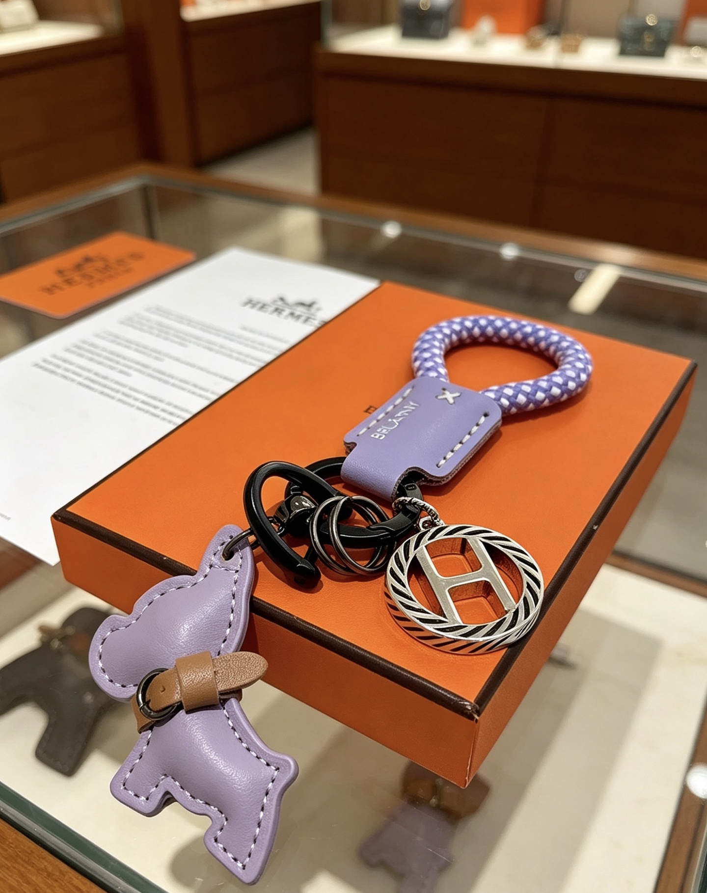 Hermes Rodeo H Logo Key Charm colgante Cuero morado lila Cordón trenzado morado y blanco Detalle de cuero bronceado Metal en tono plateado con detalles de esmalte negro Longitud total de 10 cm
