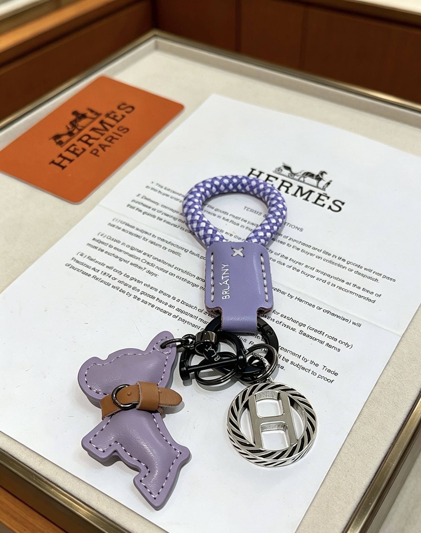 Hermes Rodeo H Logo Key Charm colgante Cuero morado lila Cordón trenzado morado y blanco Detalle de cuero bronceado Metal en tono plateado con detalles de esmalte negro Longitud total de 10 cm