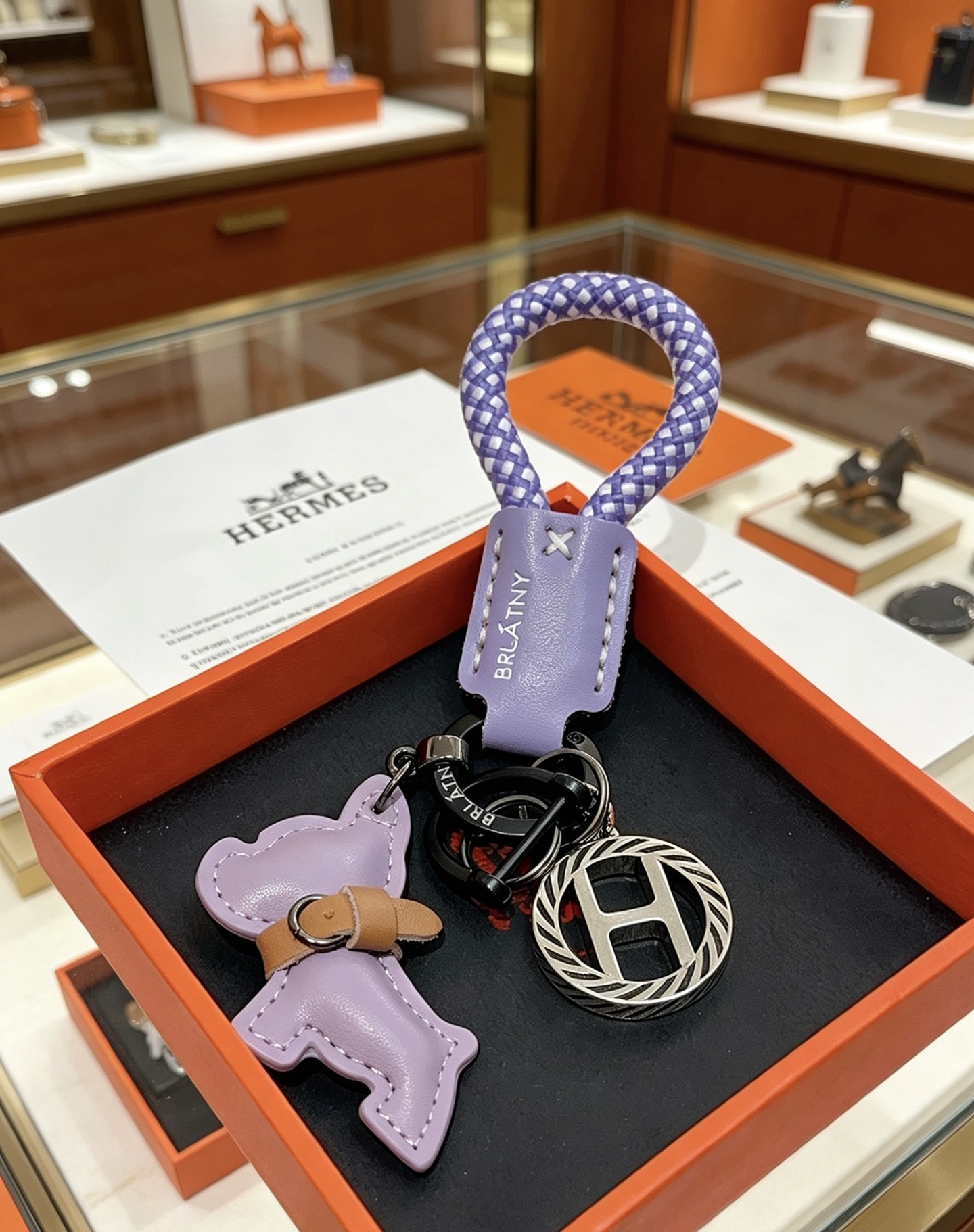 Hermes Rodeo H Logo Key Charm colgante Cuero morado lila Cordón trenzado morado y blanco Detalle de cuero bronceado Metal en tono plateado con detalles de esmalte negro Longitud total de 10 cm