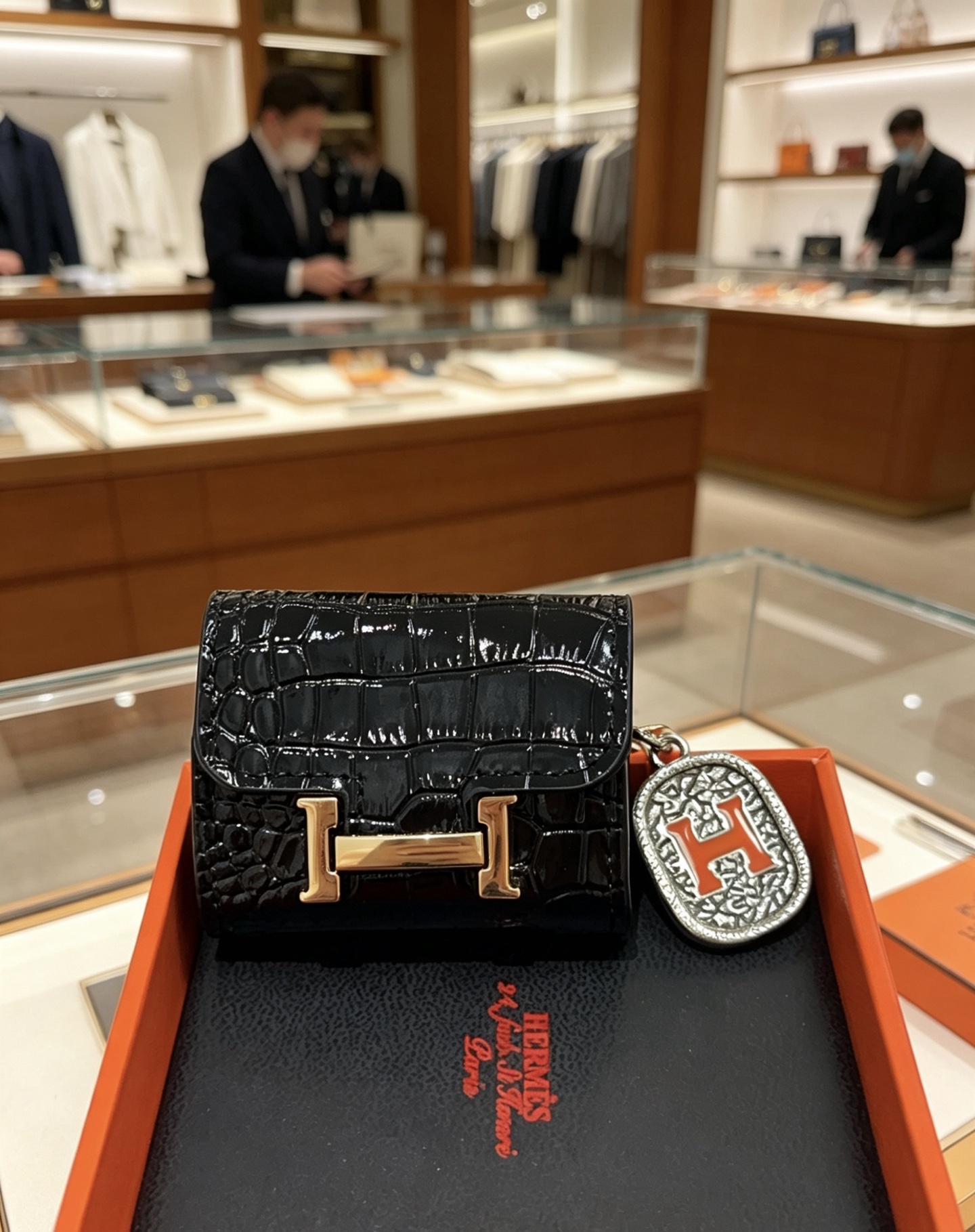 Hermes Constance Custodia per AirPods Borsa Ciondolo con ciondolo Pelle verniciata nera goffrata in coccodrillo Hardware in metallo color oro Ciondolo in metallo color argento con dettaglio H in smalto arancione Taglia unica adatta al ciondolo AirPods standard, lunghezza totale circa 8 cm